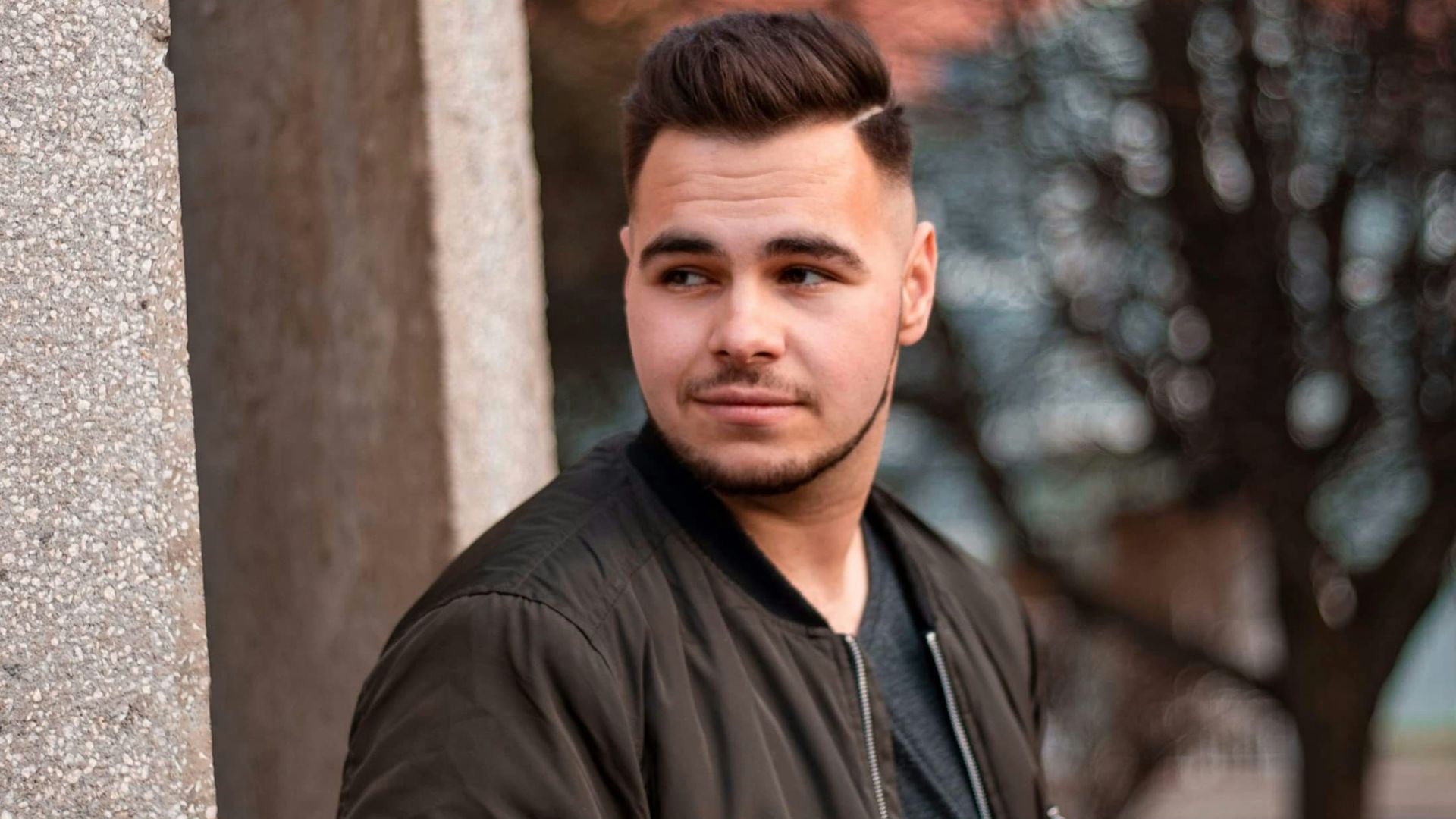 man in black leather jacket standing beside brown concrete wall during daytime
