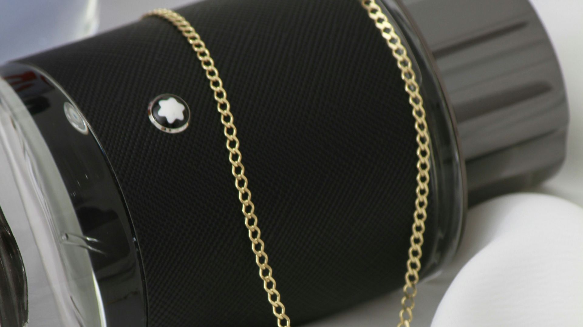 A cross pendant on a chain next to a cup