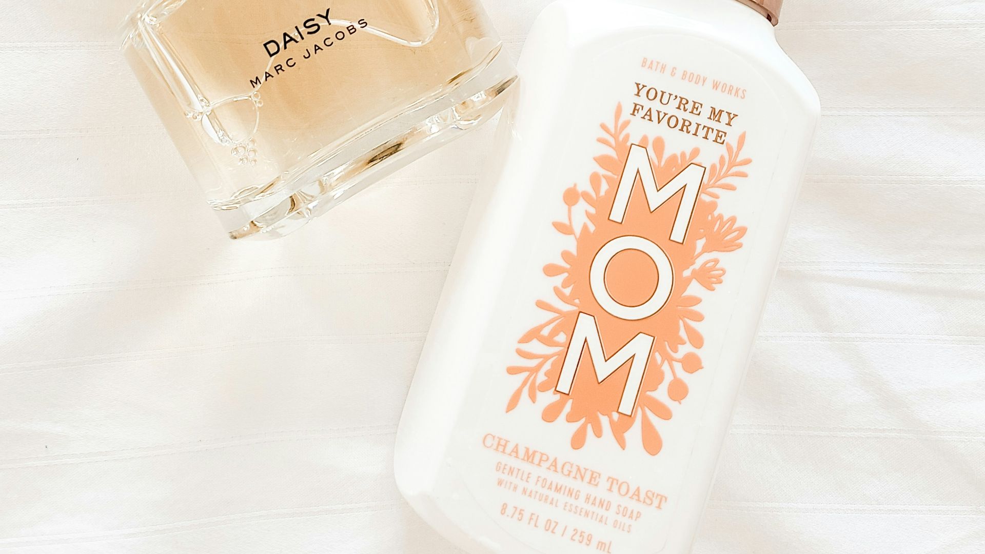 a bottle of perfume next to a flower on a bed