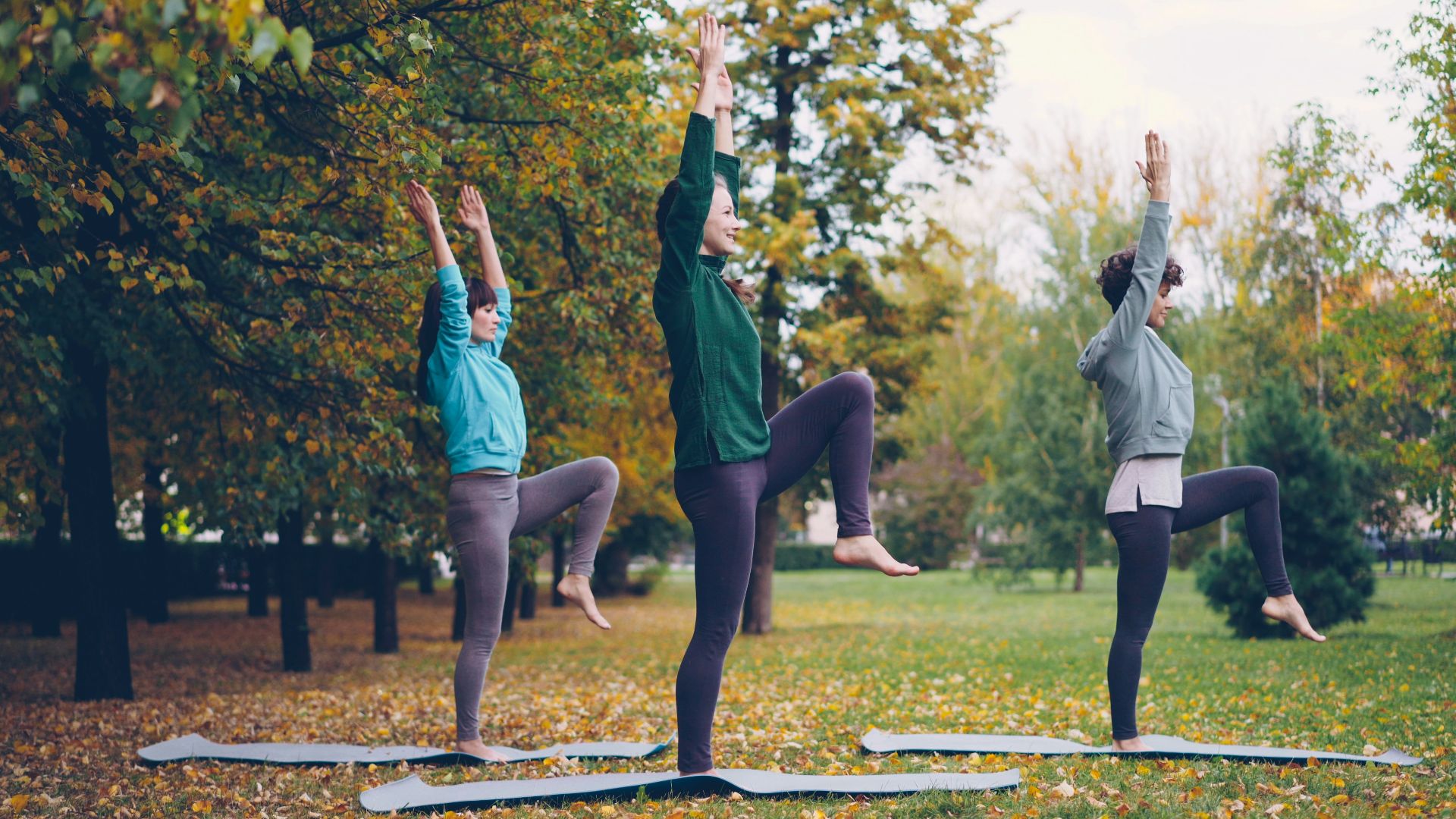 Three women practicing yoga in a park.