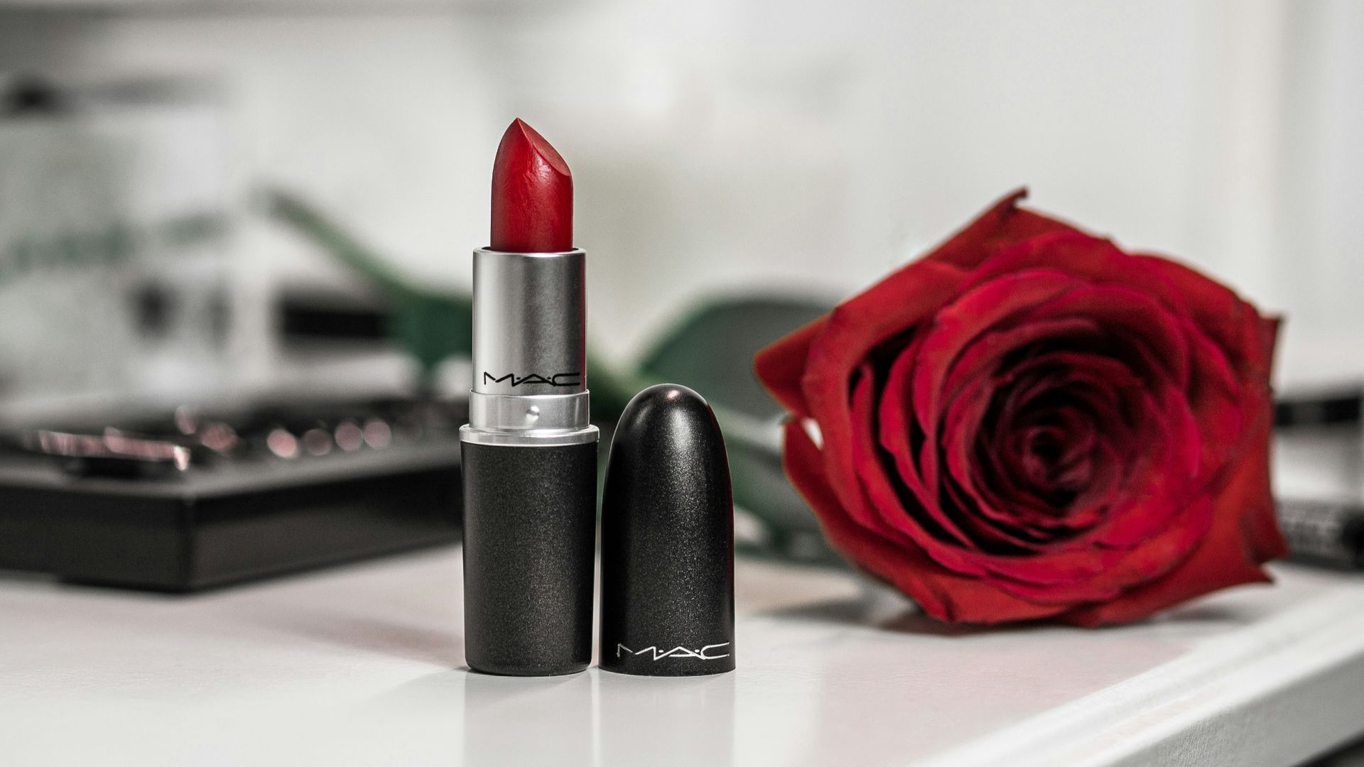 a close up of a lipstick and a rose on a table