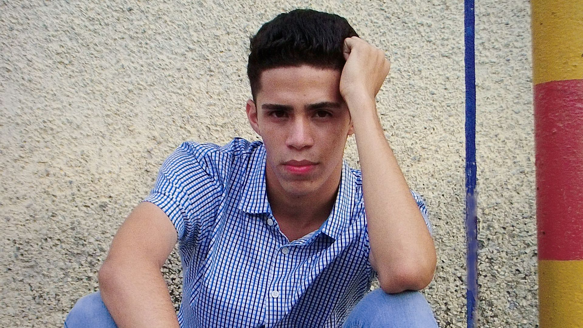 man in blue and white checkered button up shirt and blue denim jeans sitting on concrete