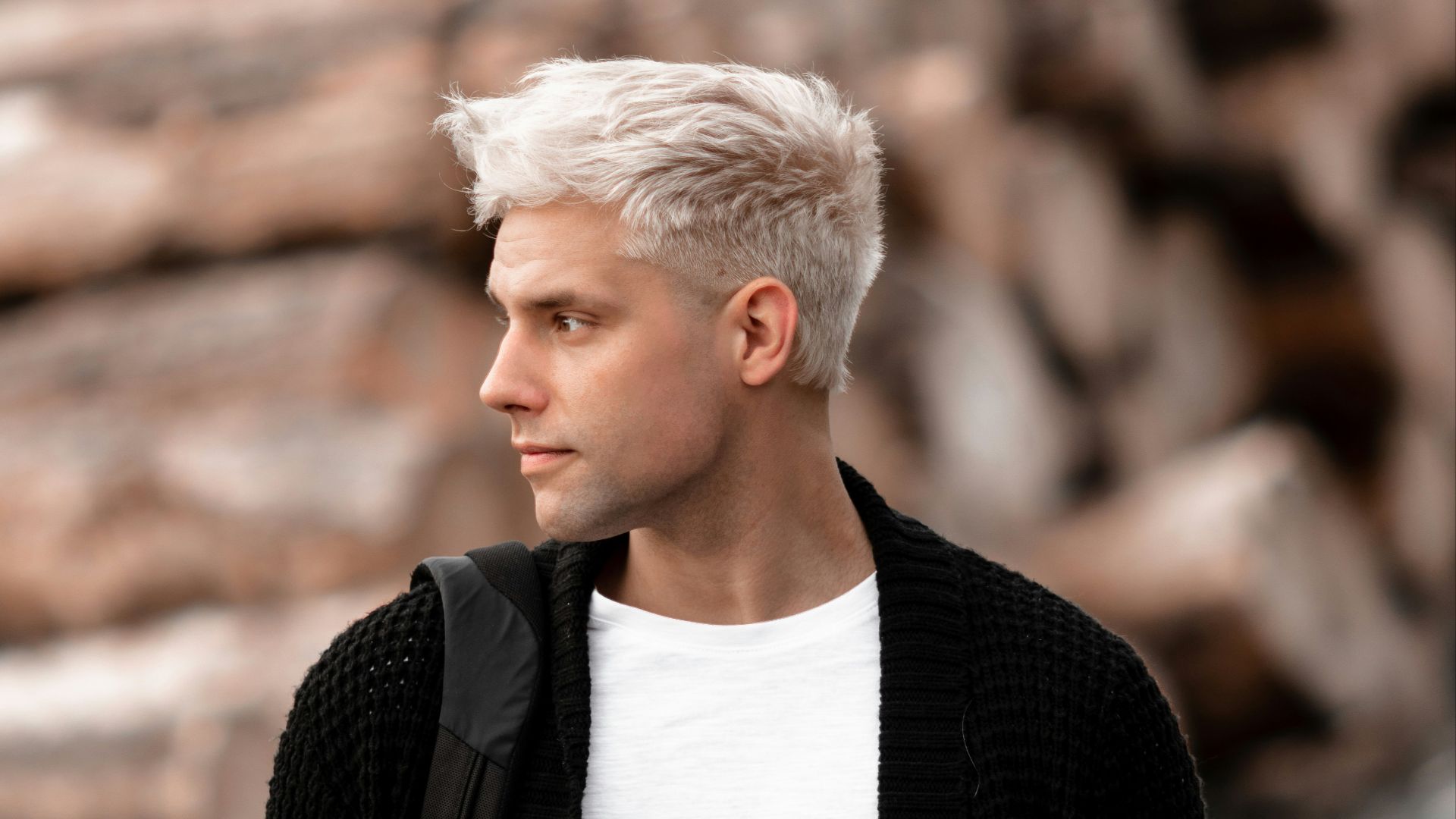 a man with white hair standing in front of a pile of logs