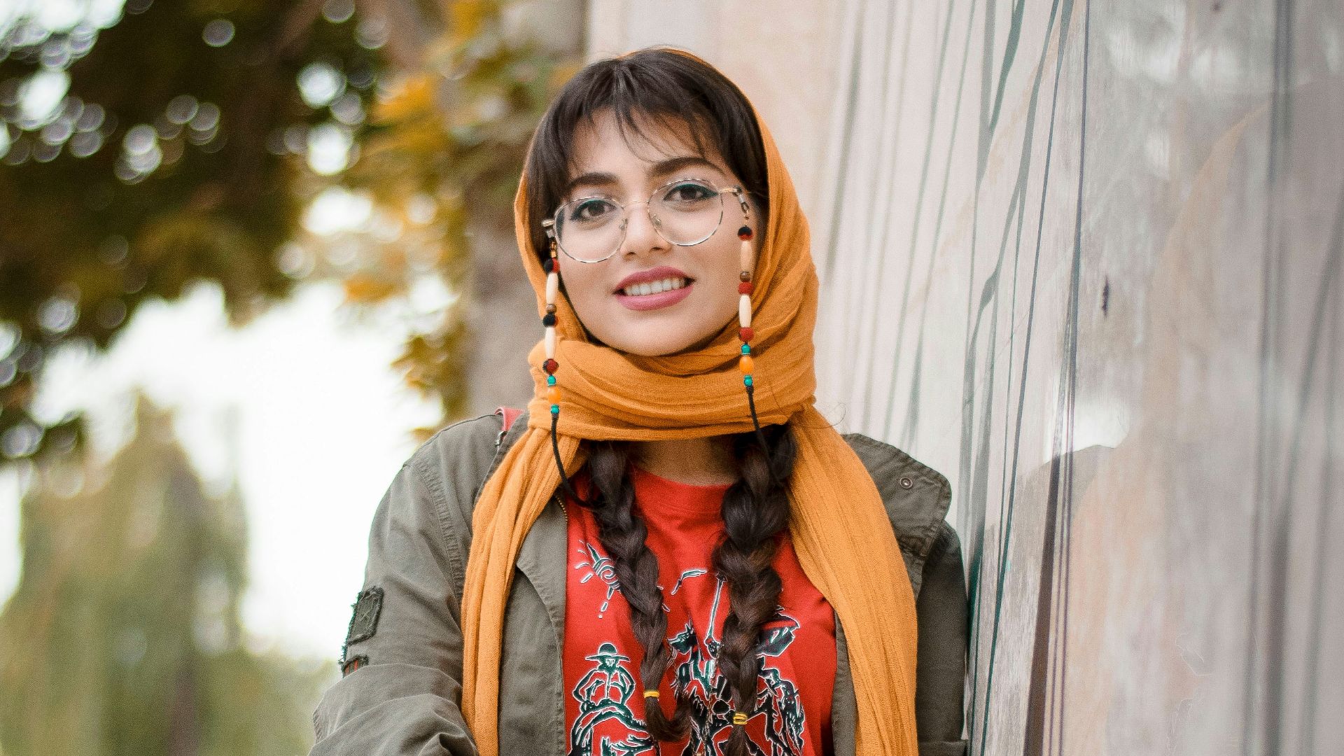 woman in gray scarf and brown coat standing beside gray wall