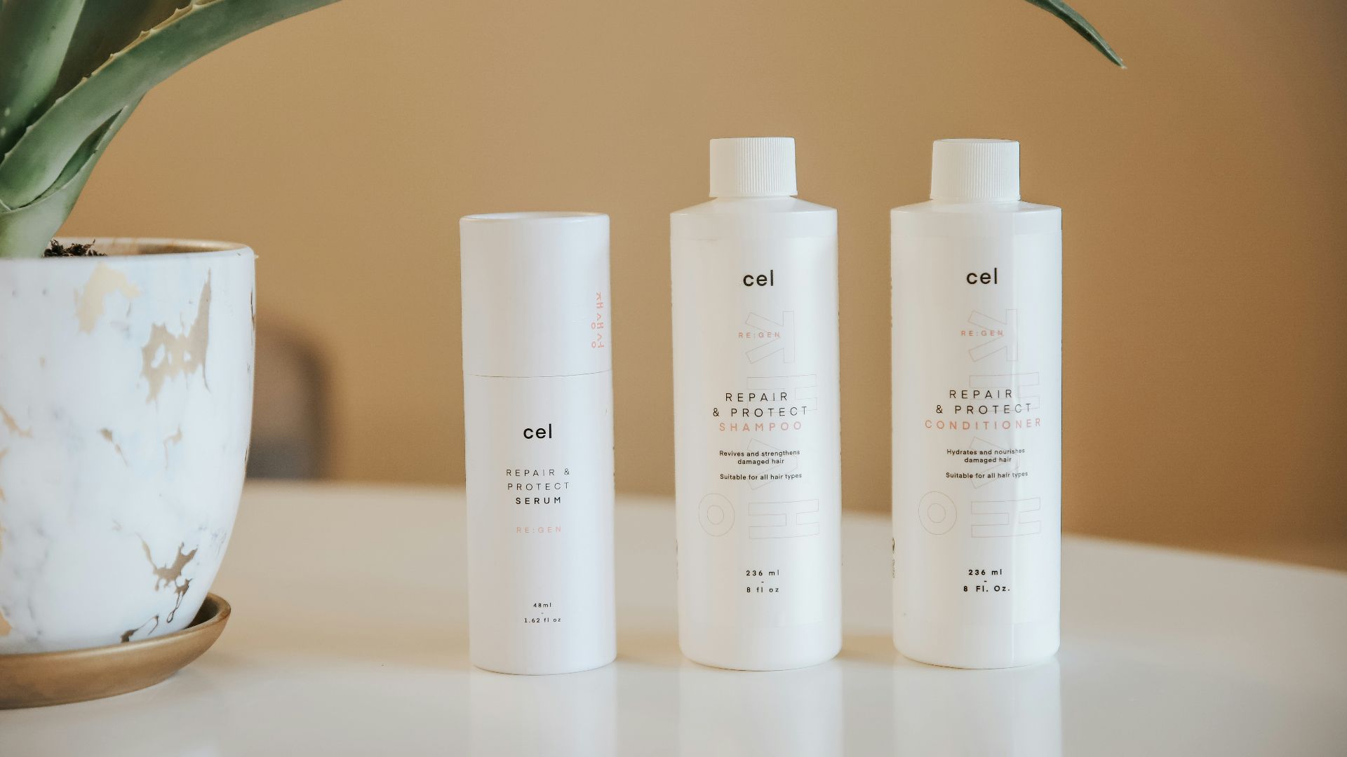 three bottles of lotion sitting on a table next to a potted plant