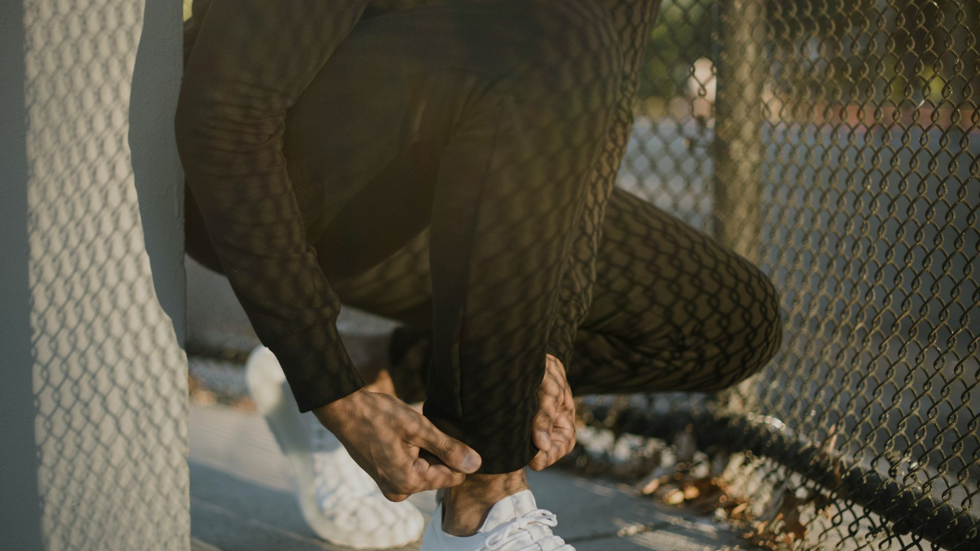 a man tying his white tennis shoes on the sidewalk