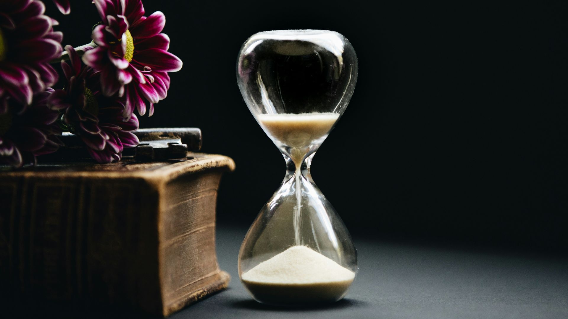 clear hour glass beside pink flowers