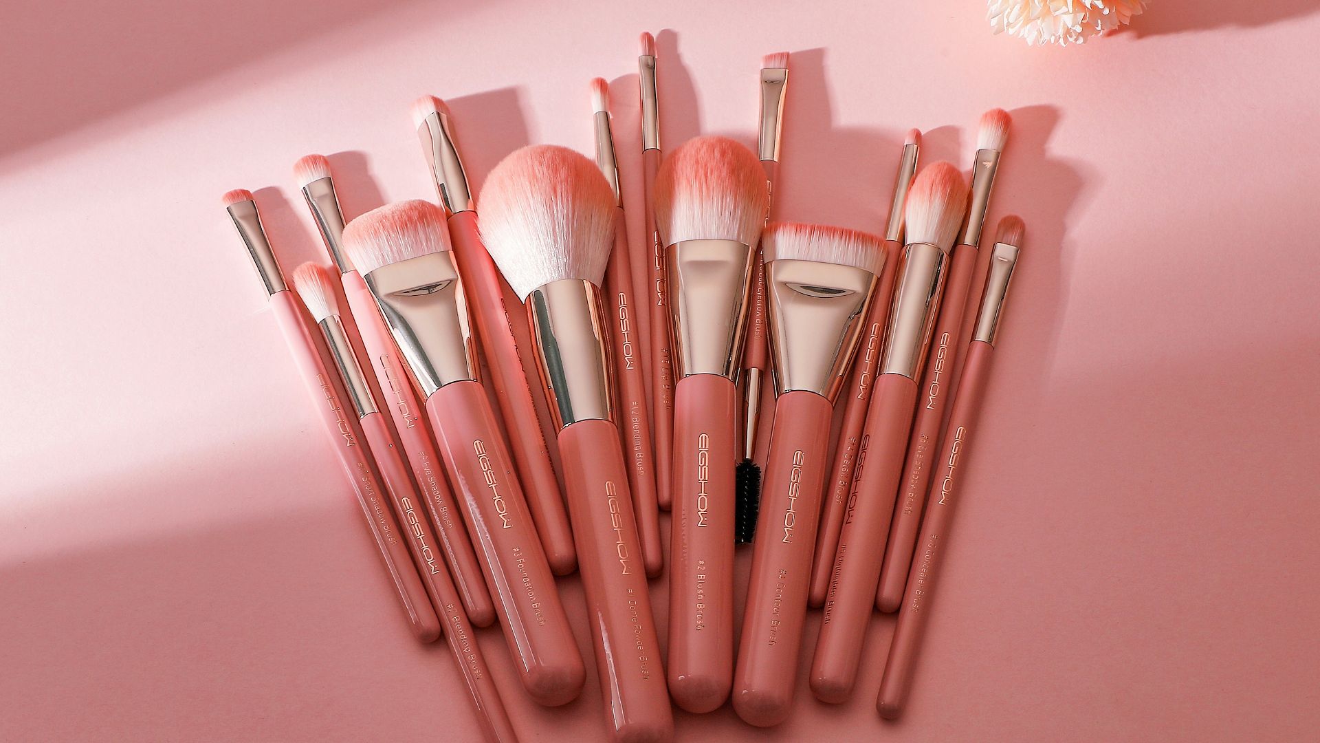 a bunch of makeup brushes sitting on top of a pink surface