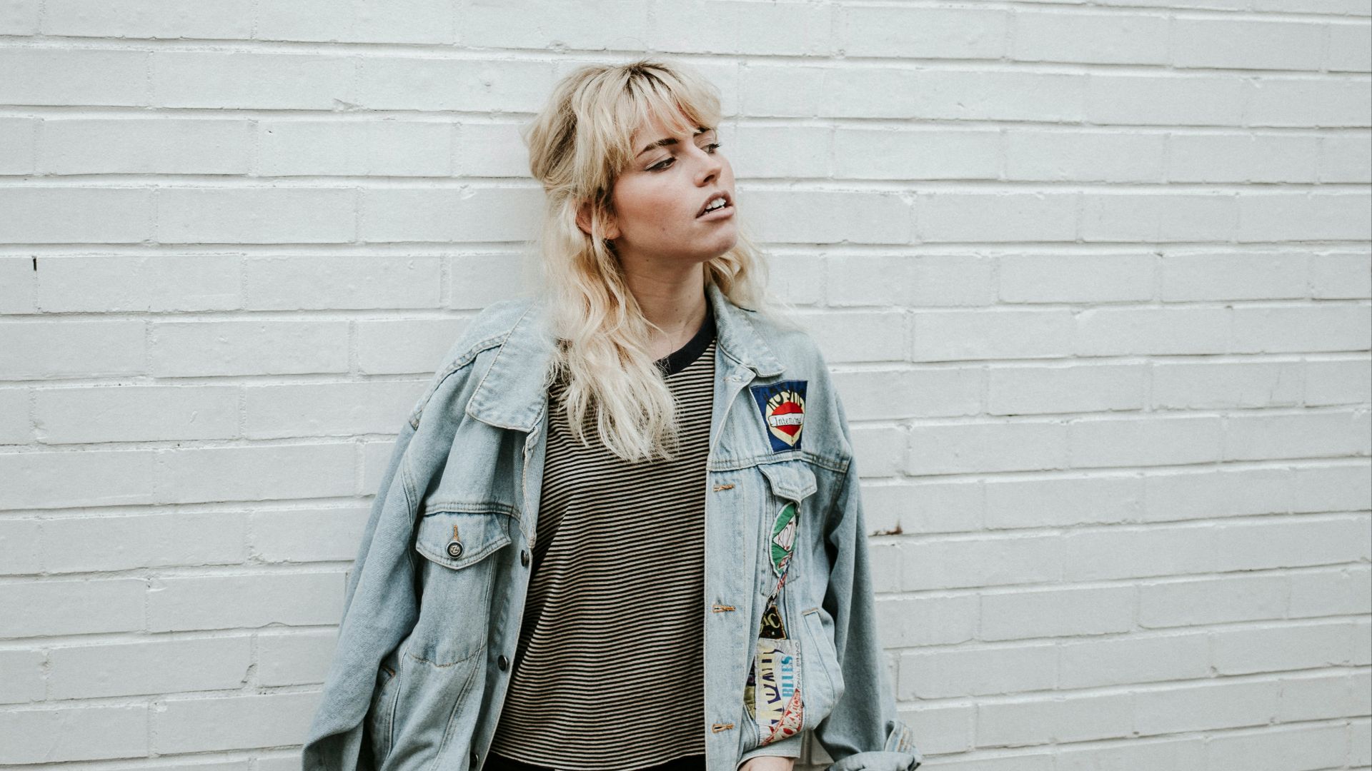 woman in blue denim jacket and black pants standing beside gray wall