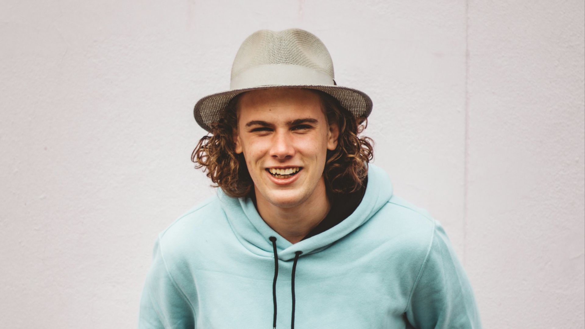 man in teal hoodie standing near white wall