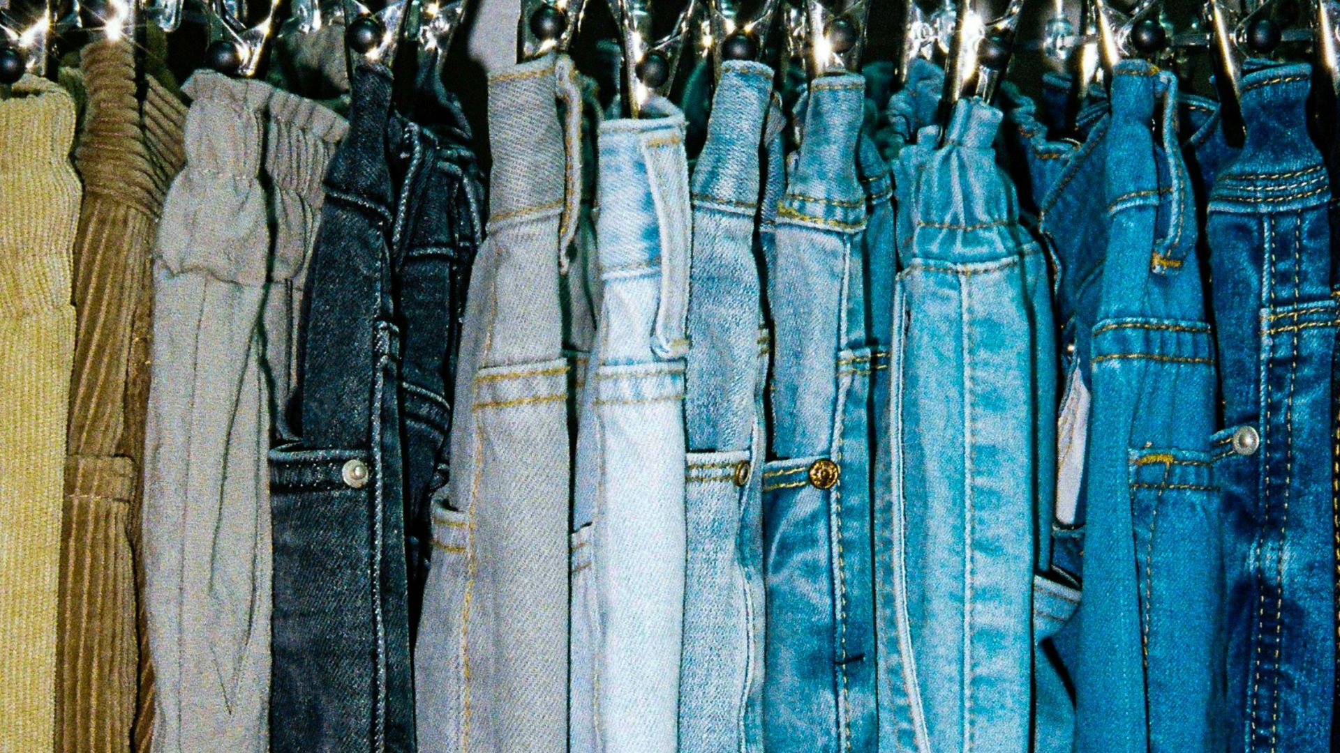 a rack of different colored jeans hanging from hooks
