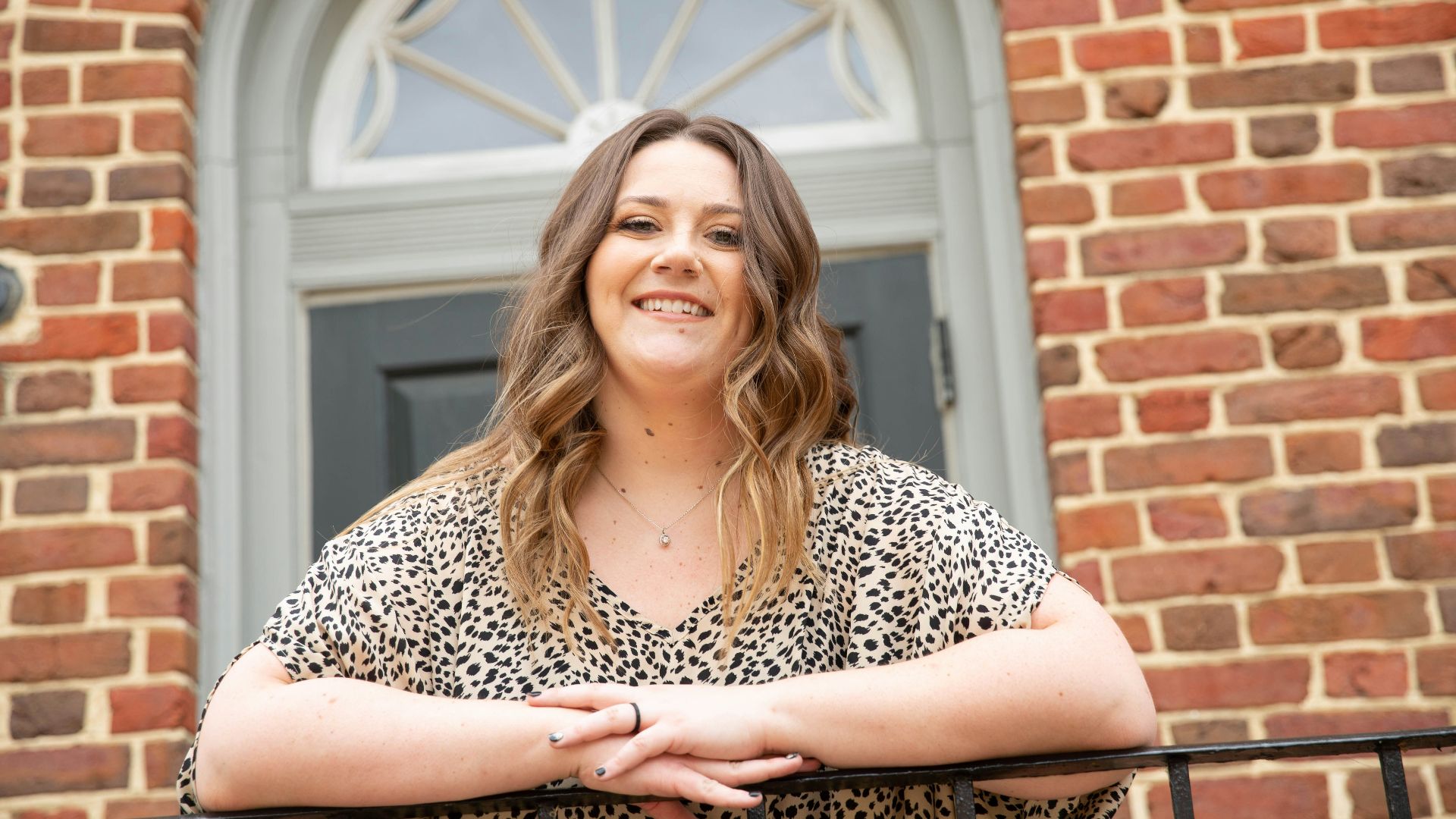 woman in black and white leopard print shirt standing near brown brick wall