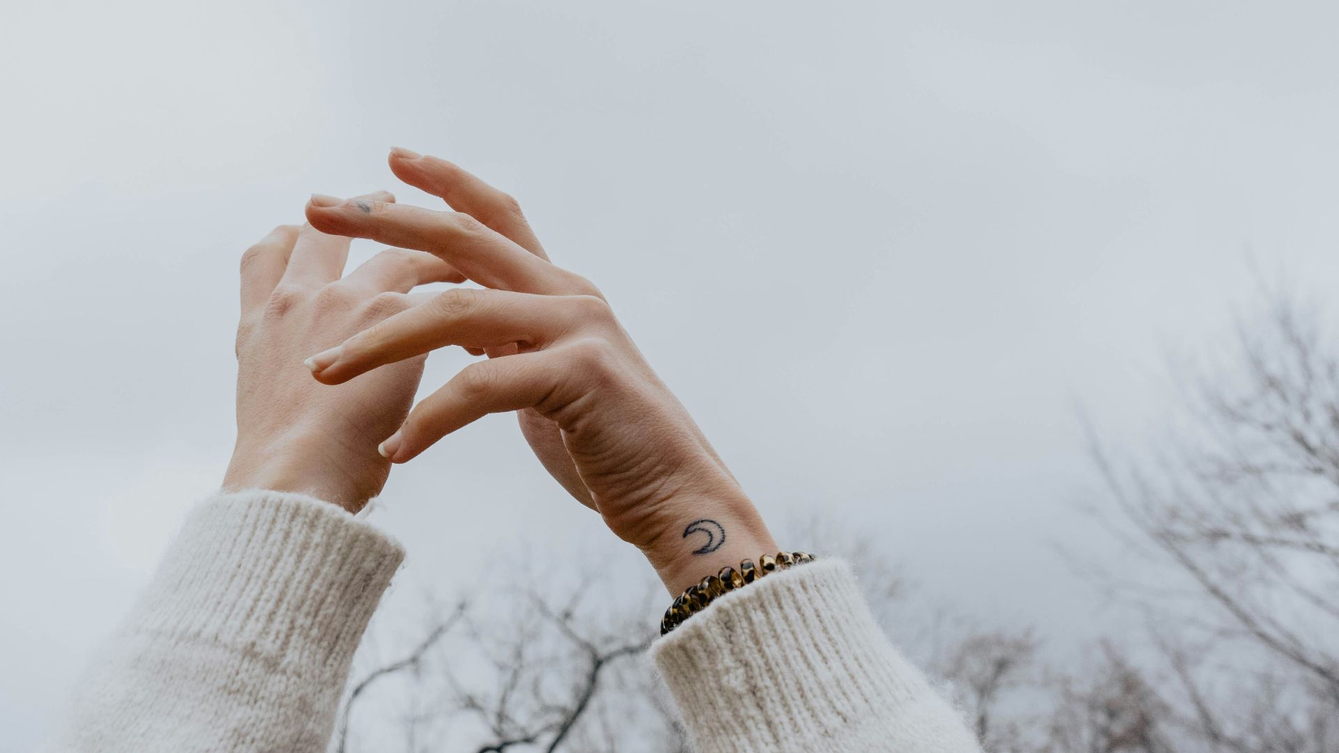 person wearing white sweater raising hands under white sky