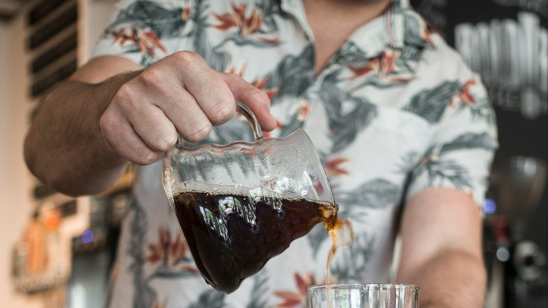 person pouring brown liquid on clear drinking glass