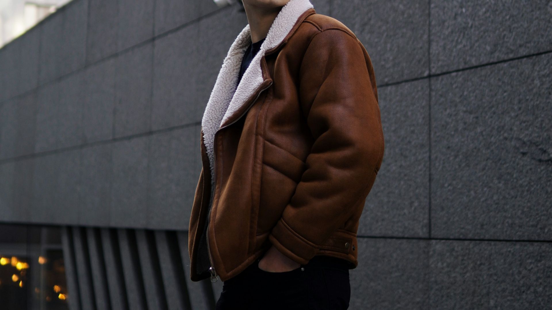 man in brown coat standing beside gray concrete wall during daytime