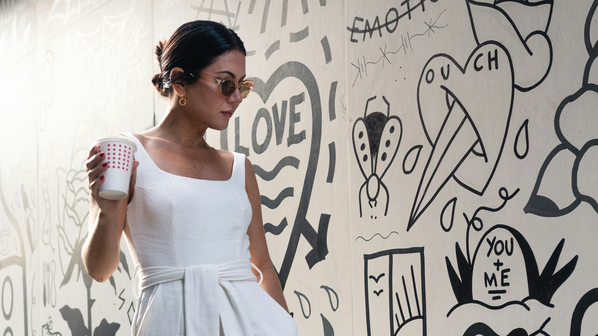 woman holding cup walking beside wall
