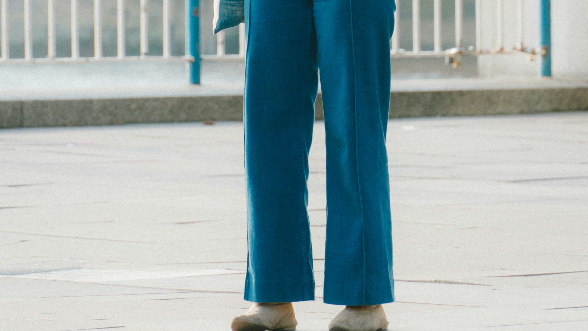 Woman in striped shirt and blue pants stands outdoors.