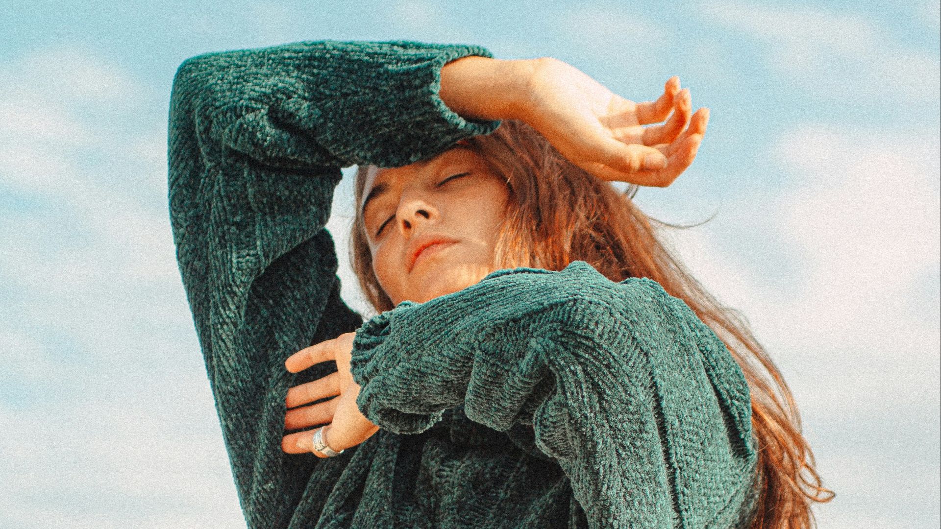 woman in blue sweater covering her face with her hand