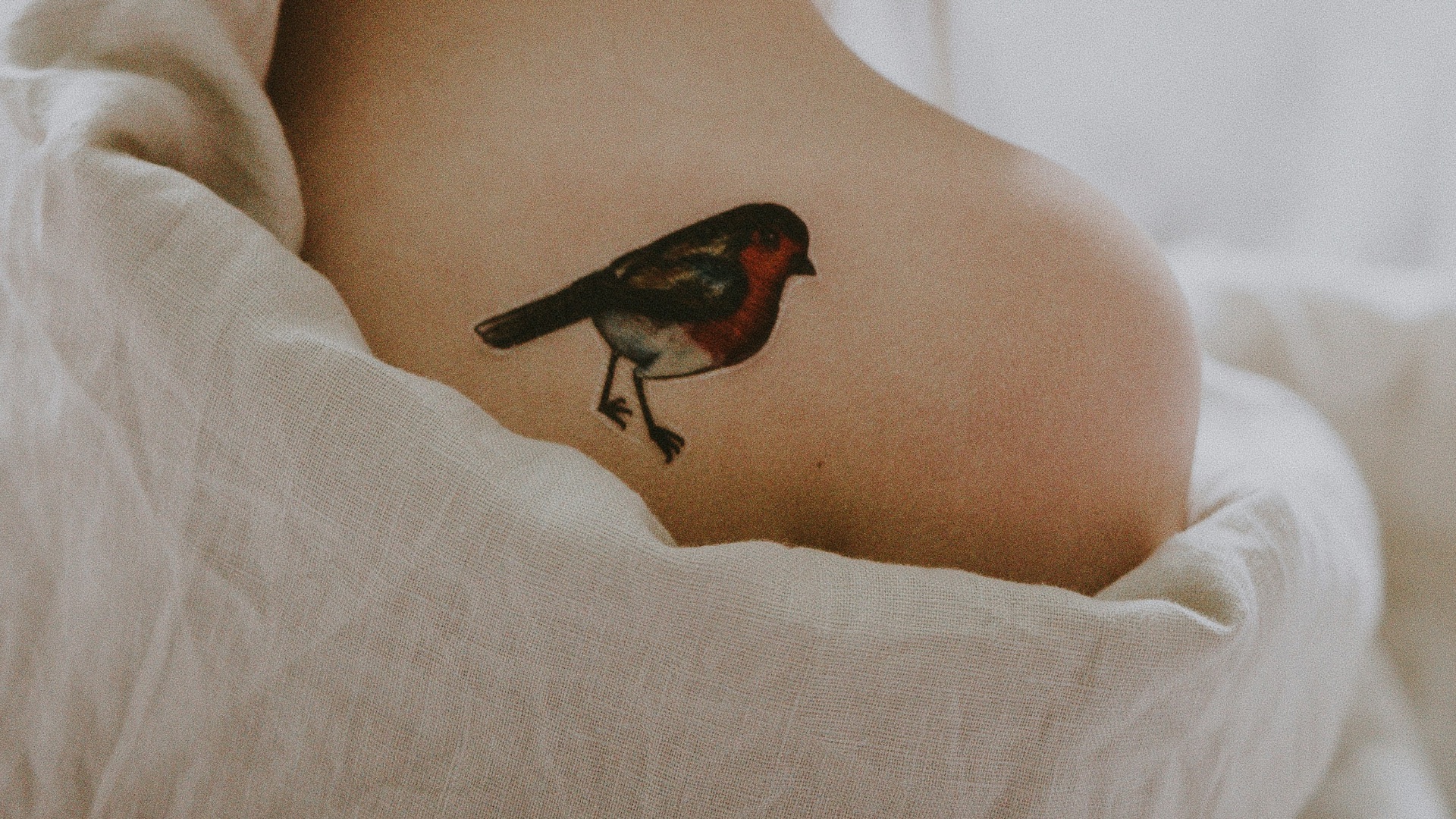 woman with bird tattoo in shoulder laying on white surface