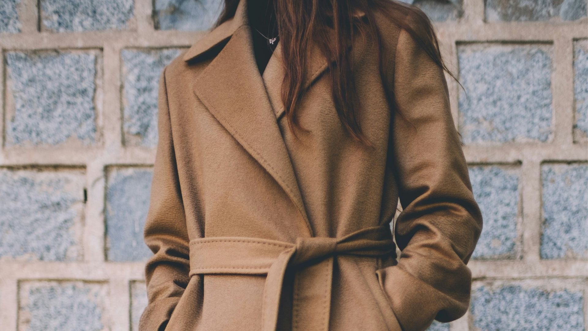 woman wearing brown single-breasted coat standing in front of gray brick wall