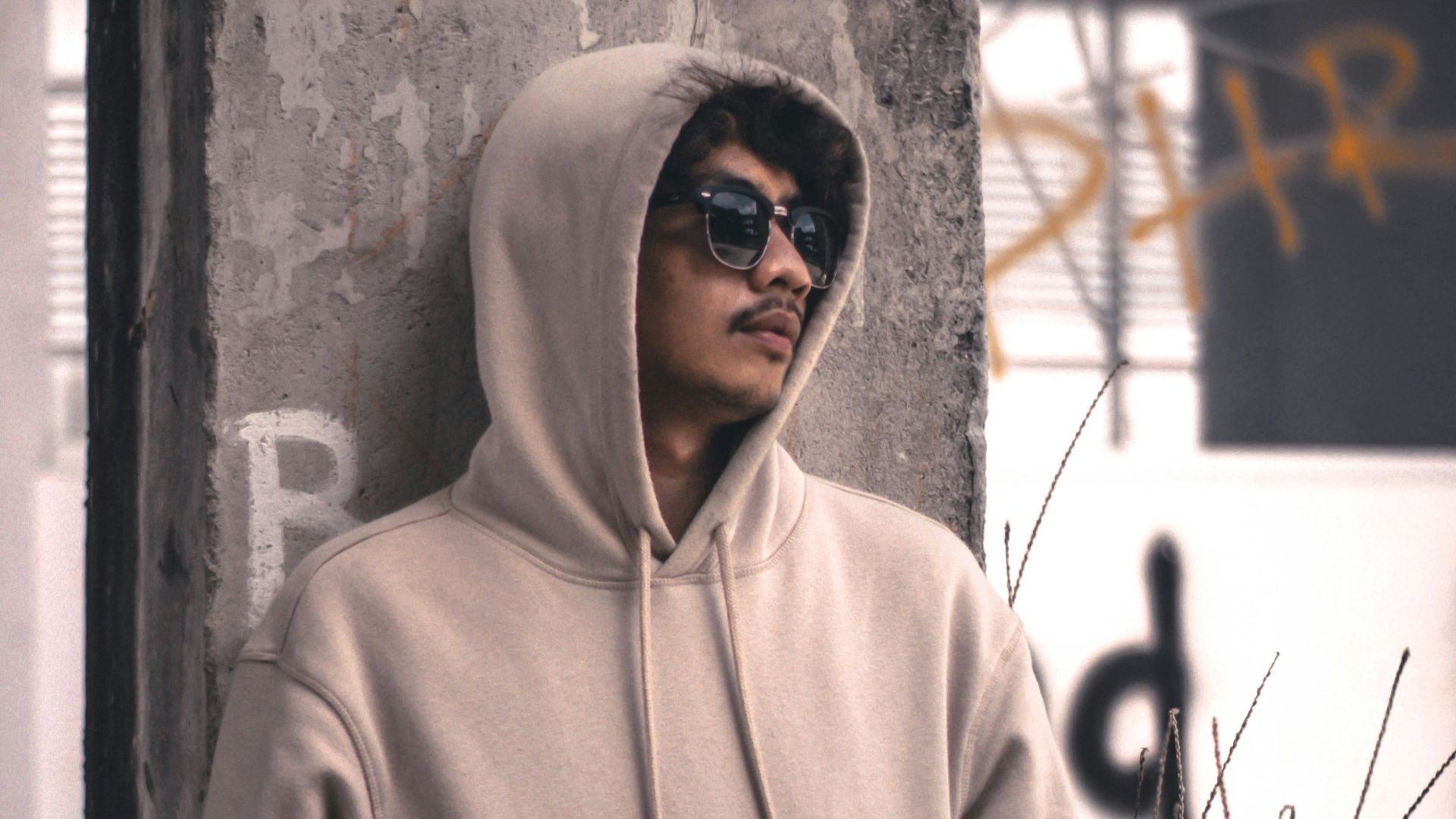 men wearing a grey hoodie jacket leaning in a wall during daytime