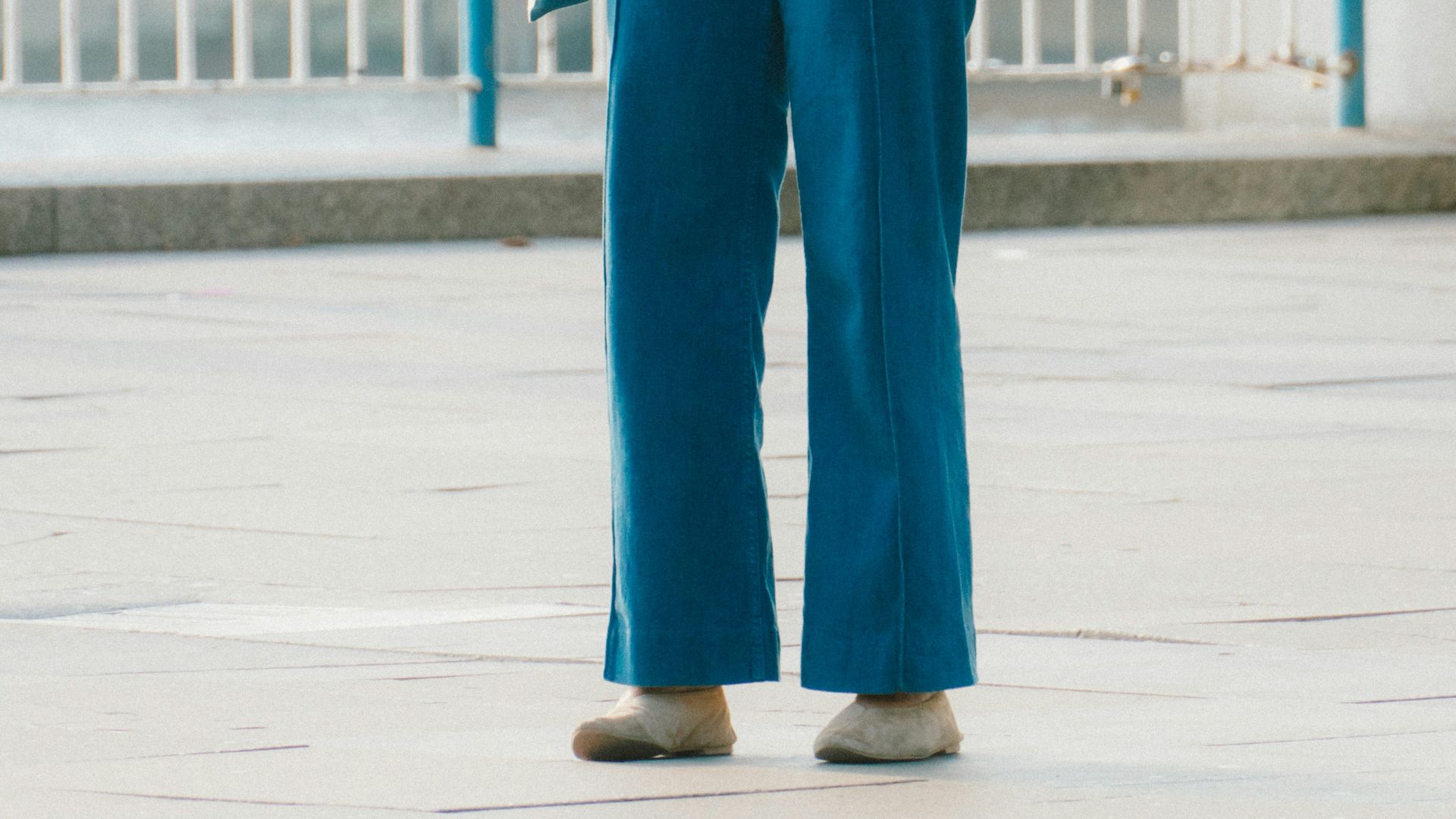 Woman in striped shirt and blue pants stands outdoors.