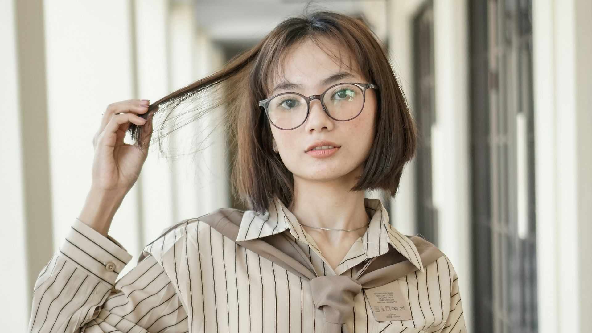 A woman wearing glasses and a tie standing in a hallway