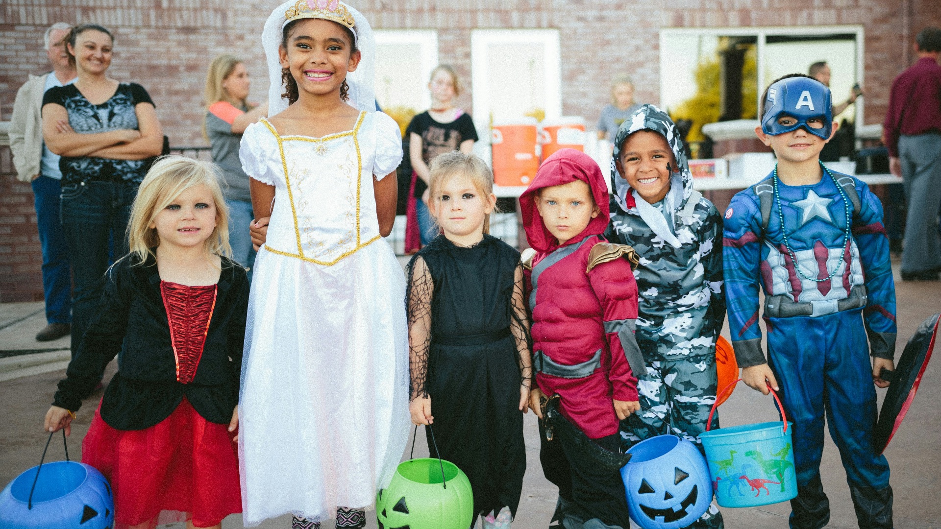 children standing while holding Jack 'o lantern and wearing costume
