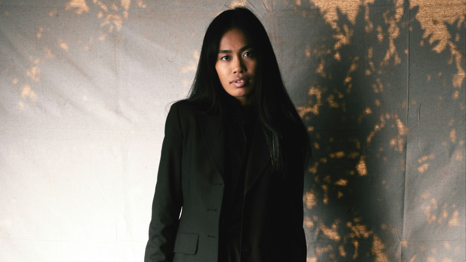 A woman stands in a black dress and jacket.