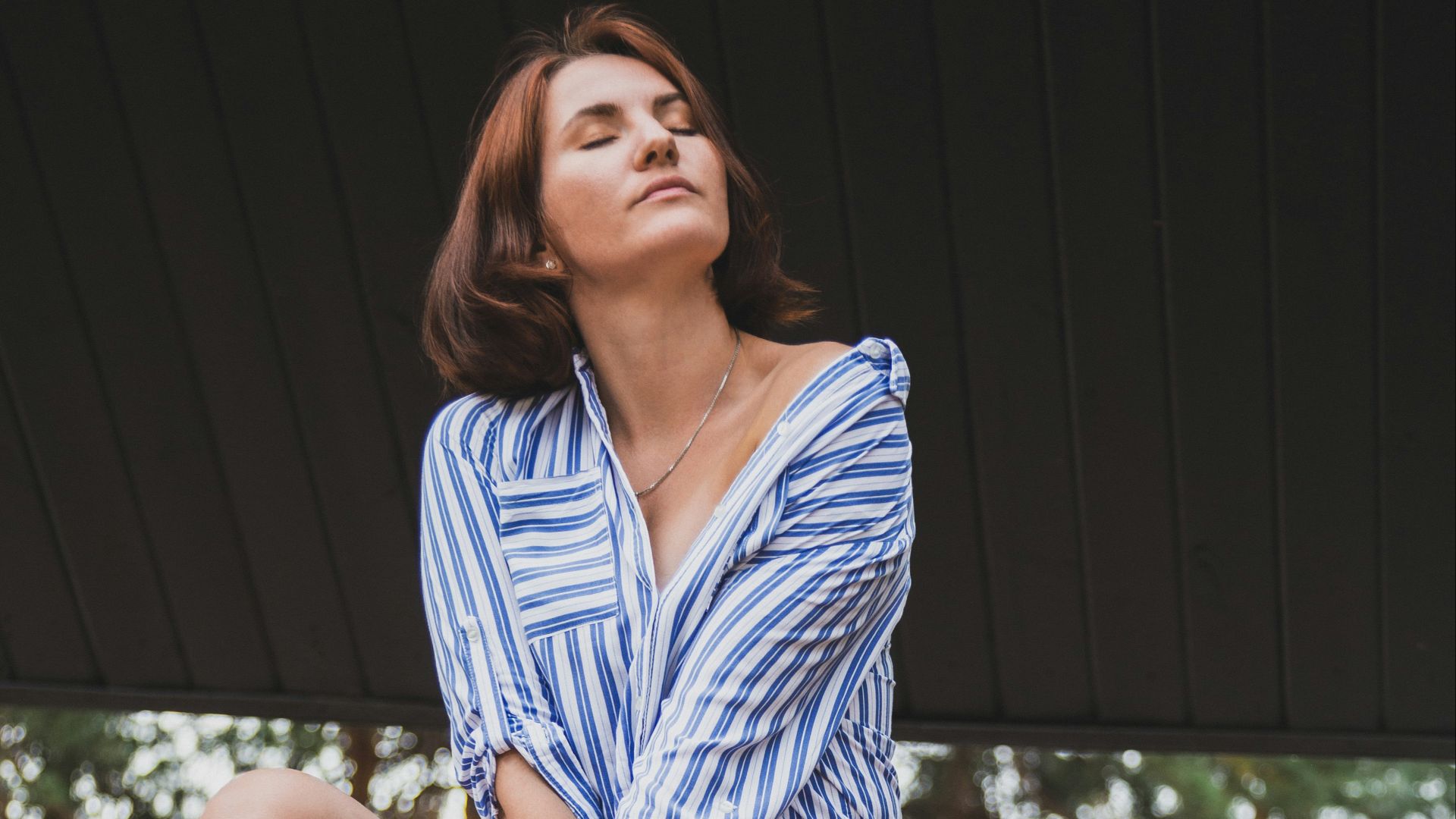 woman in blue and white stripe dress shirt sitting on brown wooden bench