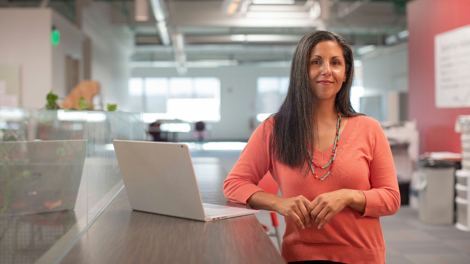 woman in orange long sleeve shirt sitting beside table with macbook pro