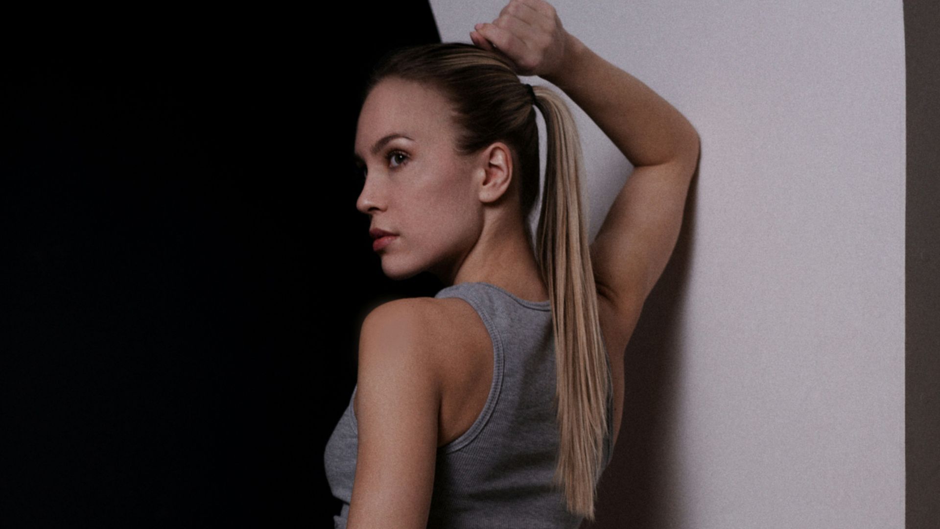 Woman in grey athletic wear leans against wall.