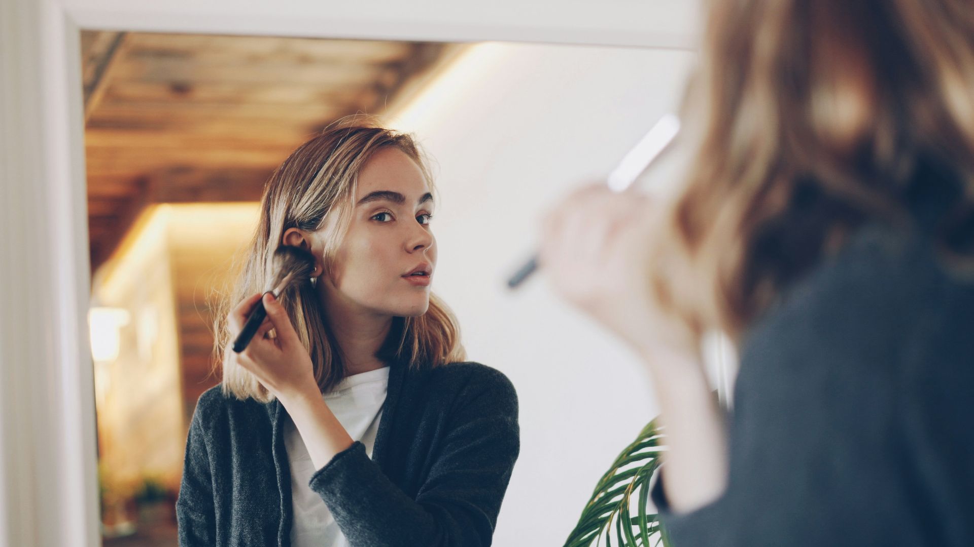 Young woman applying makeup in mirror.