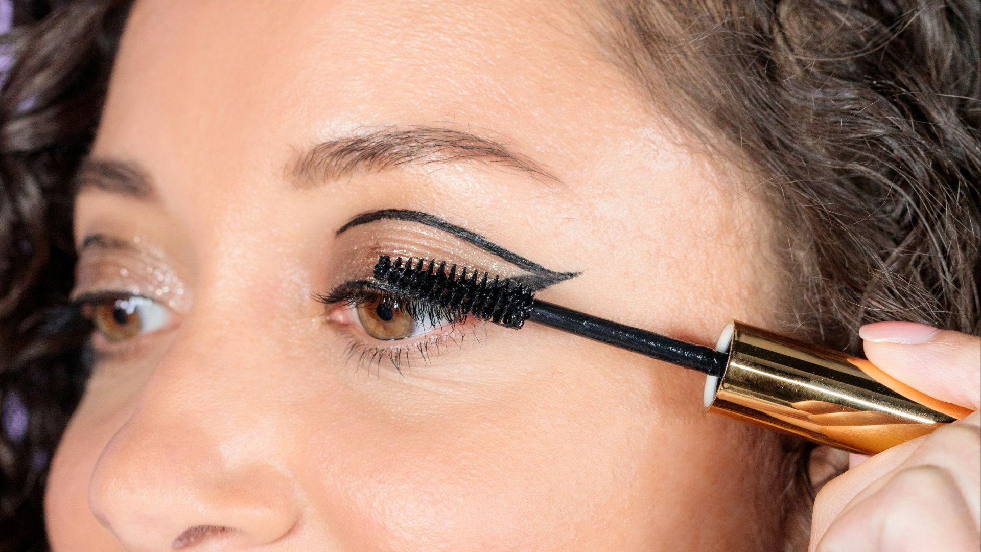 woman with black hair holding brown and black makeup brush