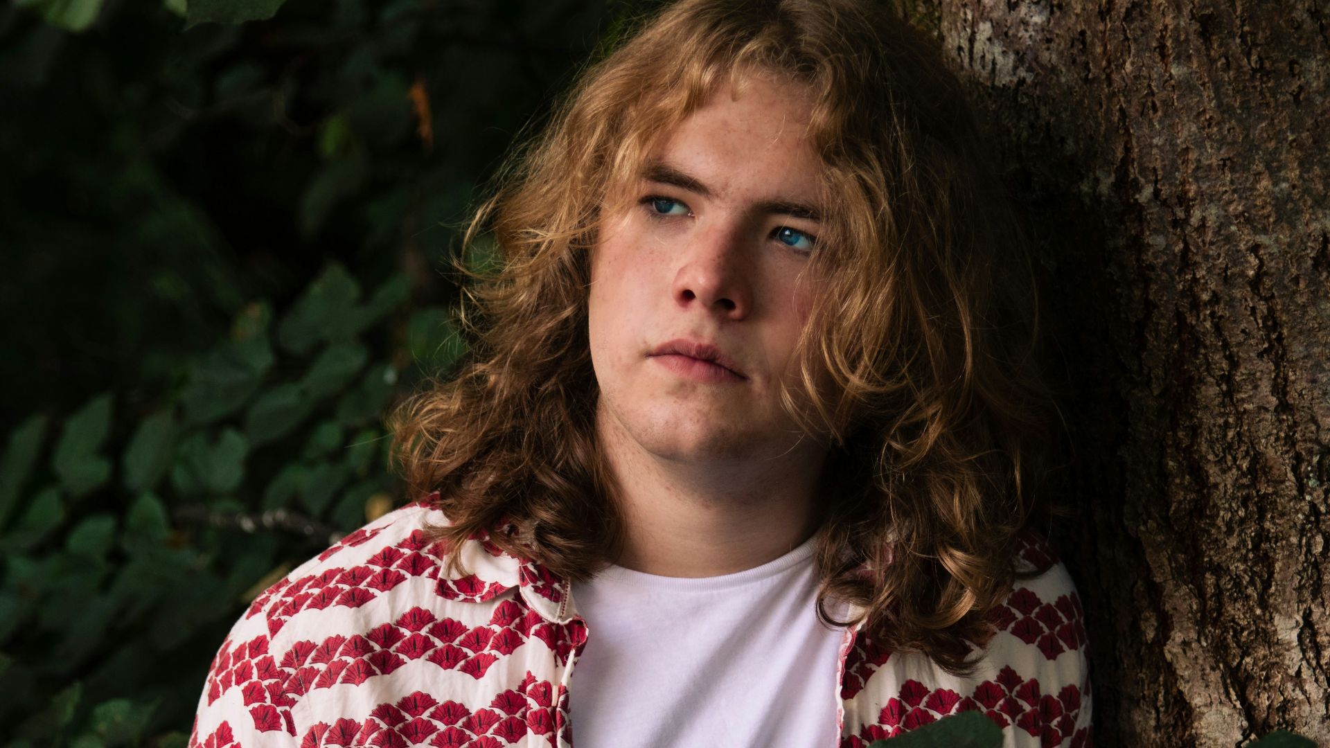 a young man leaning against a tree in a forest