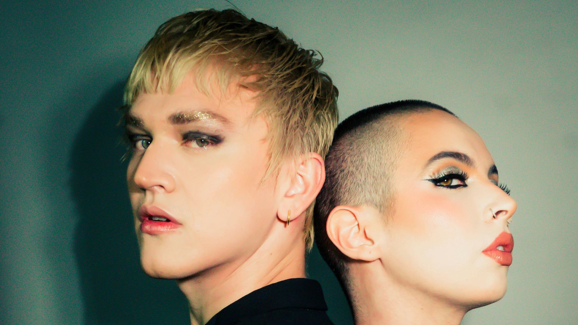 Two individuals with dramatic makeup stand back to back