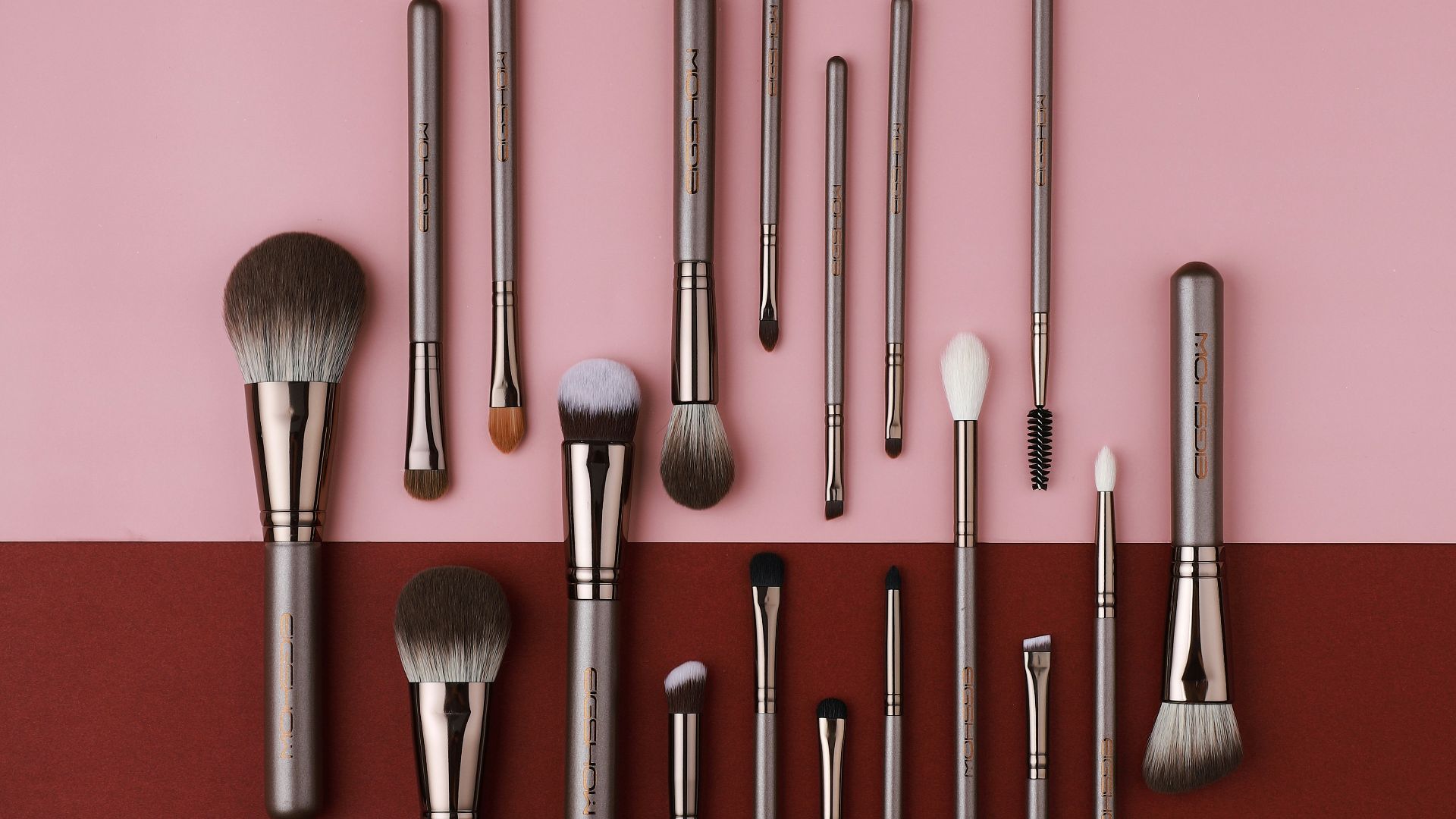 a collection of makeup brushes on a pink and red background