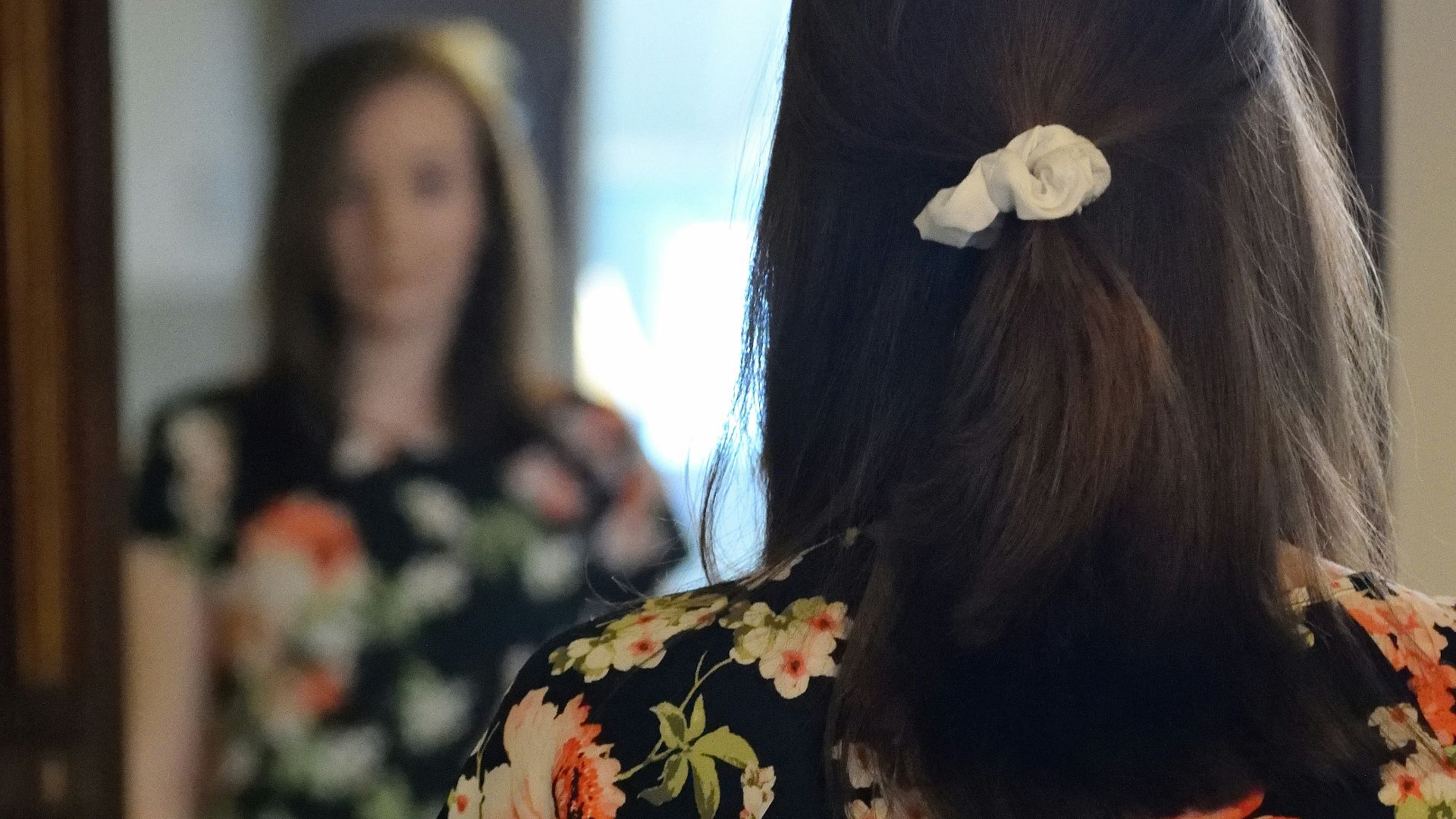 woman wearing black and multicolored blouse and blue denim jeans facing mirror inside white concrete room