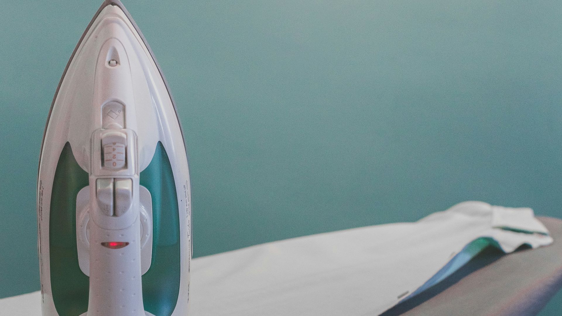 white and teal steam clothes iron plugged on ironing board