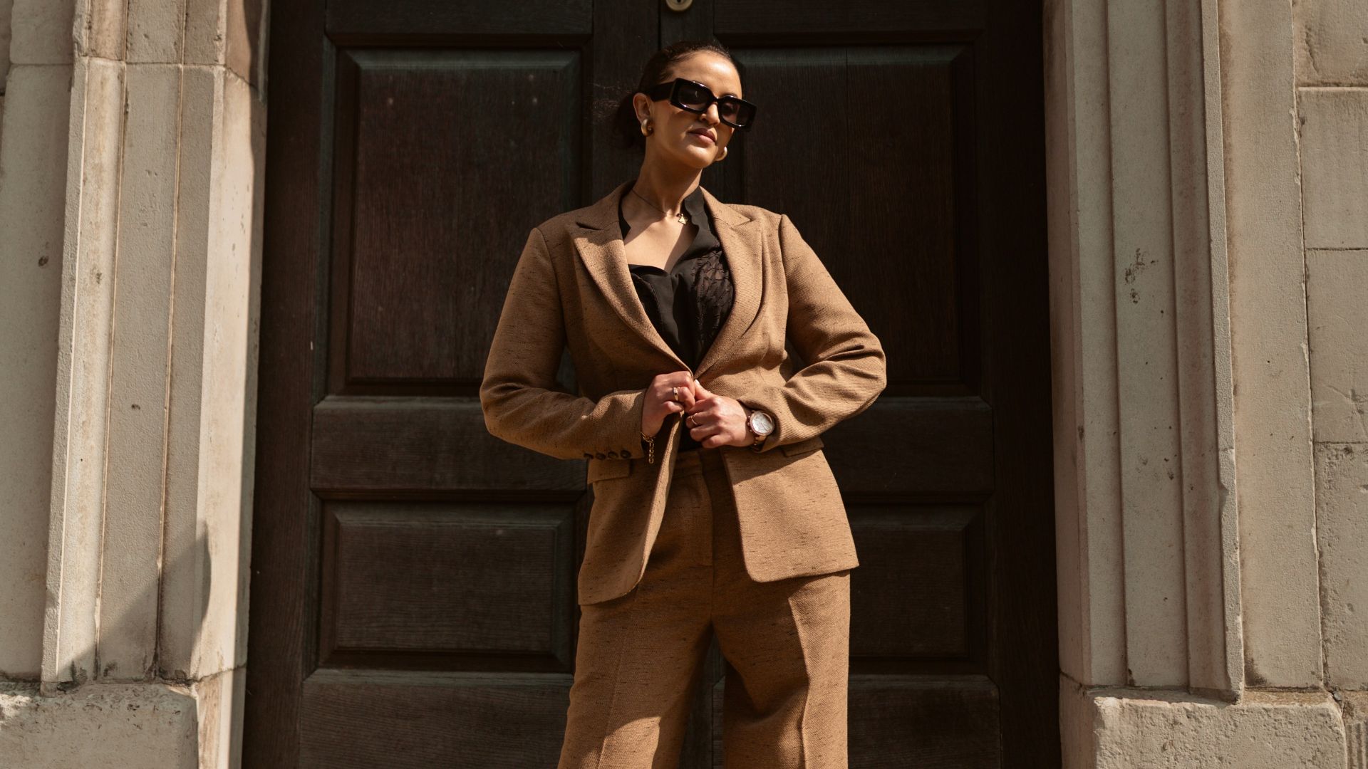 A stylish woman in a brown pantsuit poses.