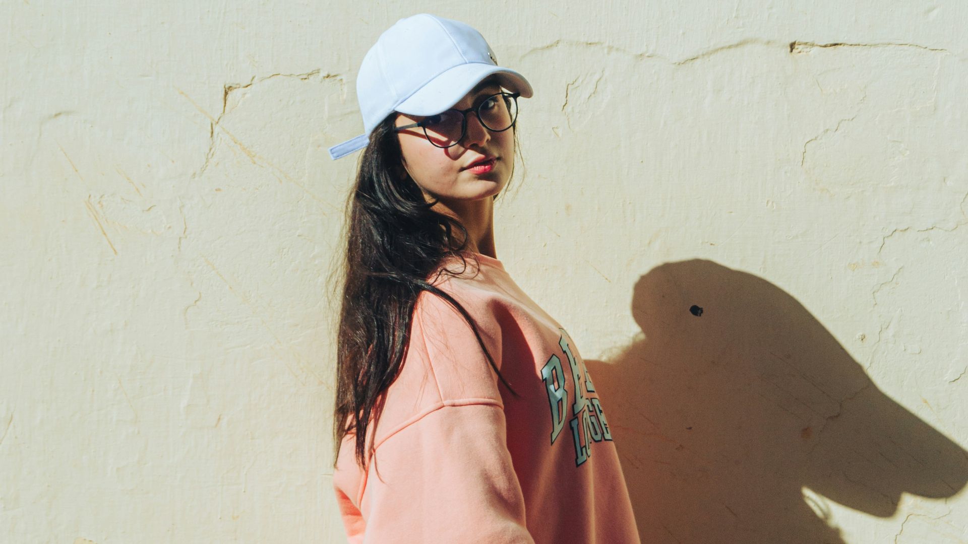 a woman standing in front of a wall wearing a hat