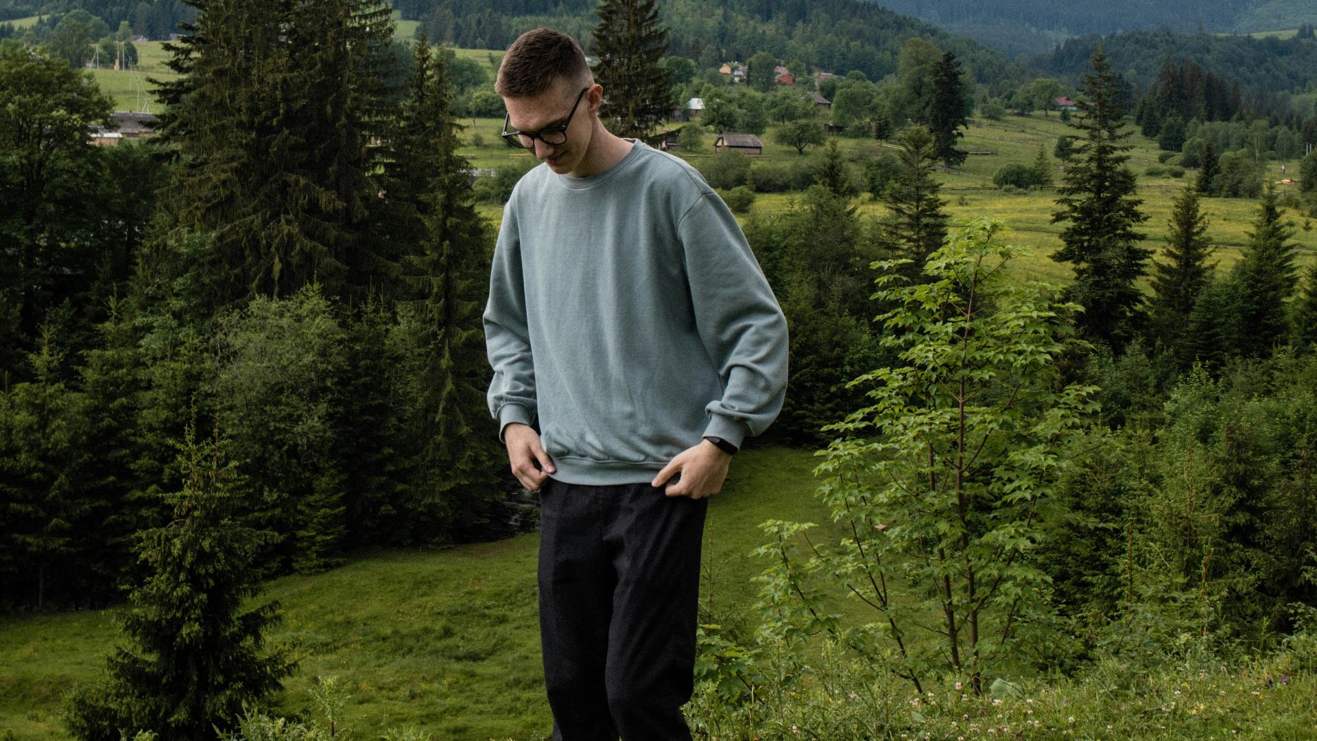 a man standing on a hill with trees and mountains in the background