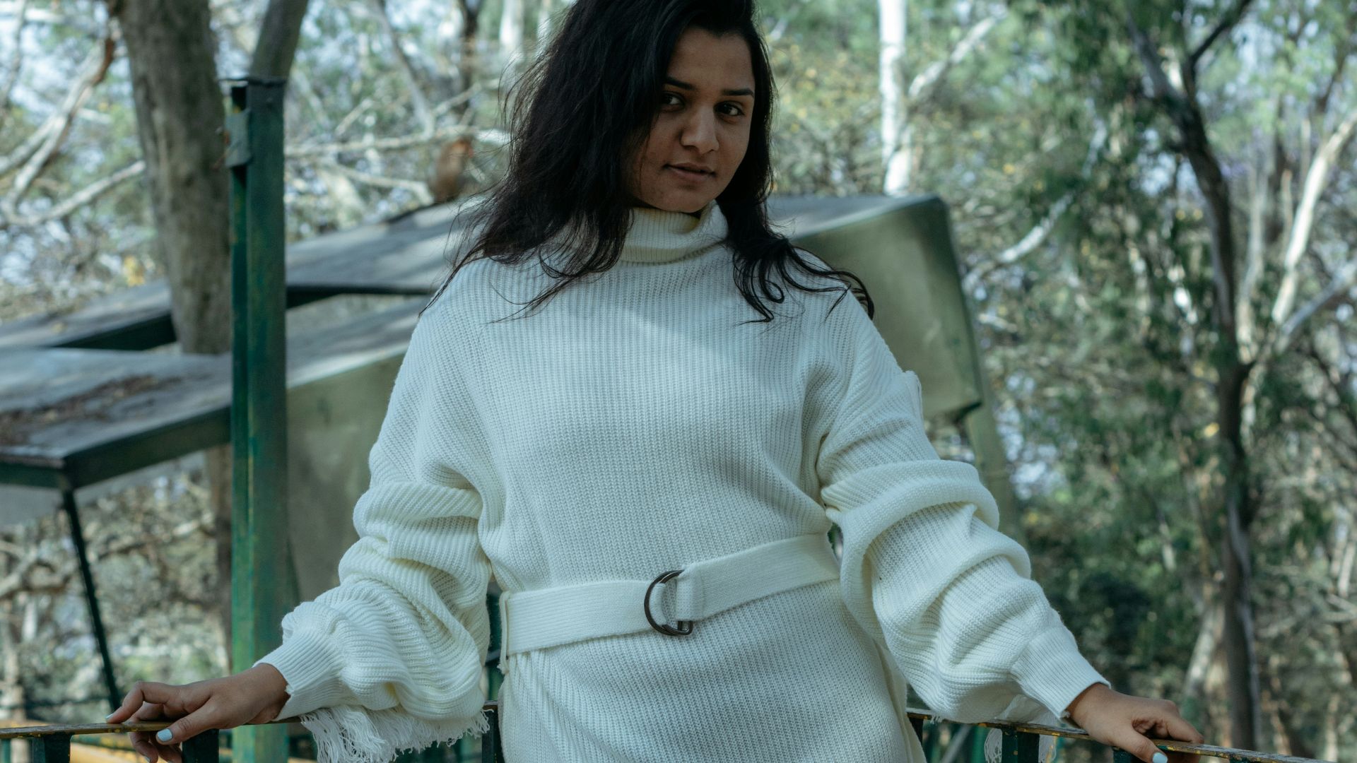 Woman poses on a bridge in a white dress.