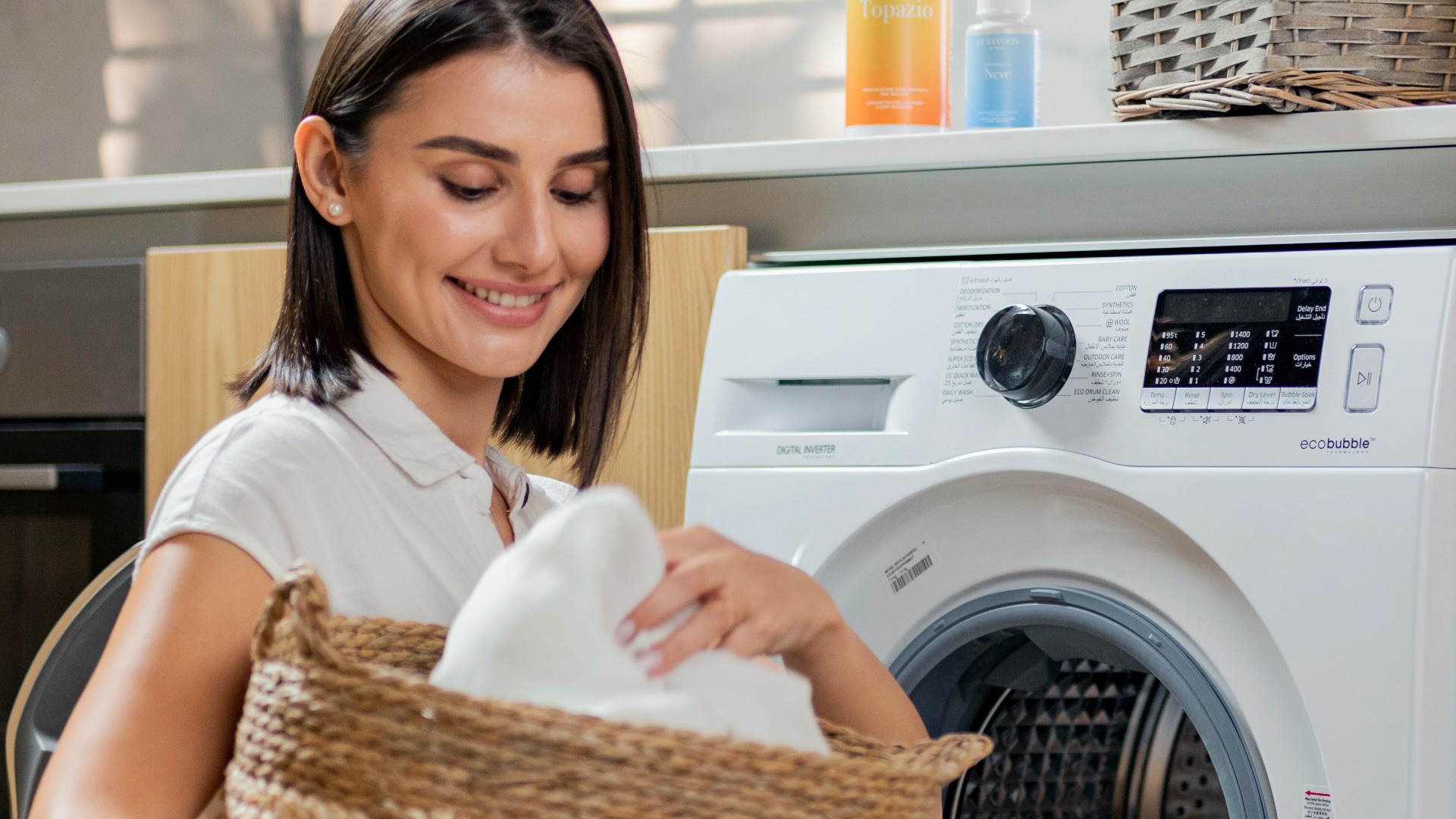 a woman is holding a basket near a washing machine