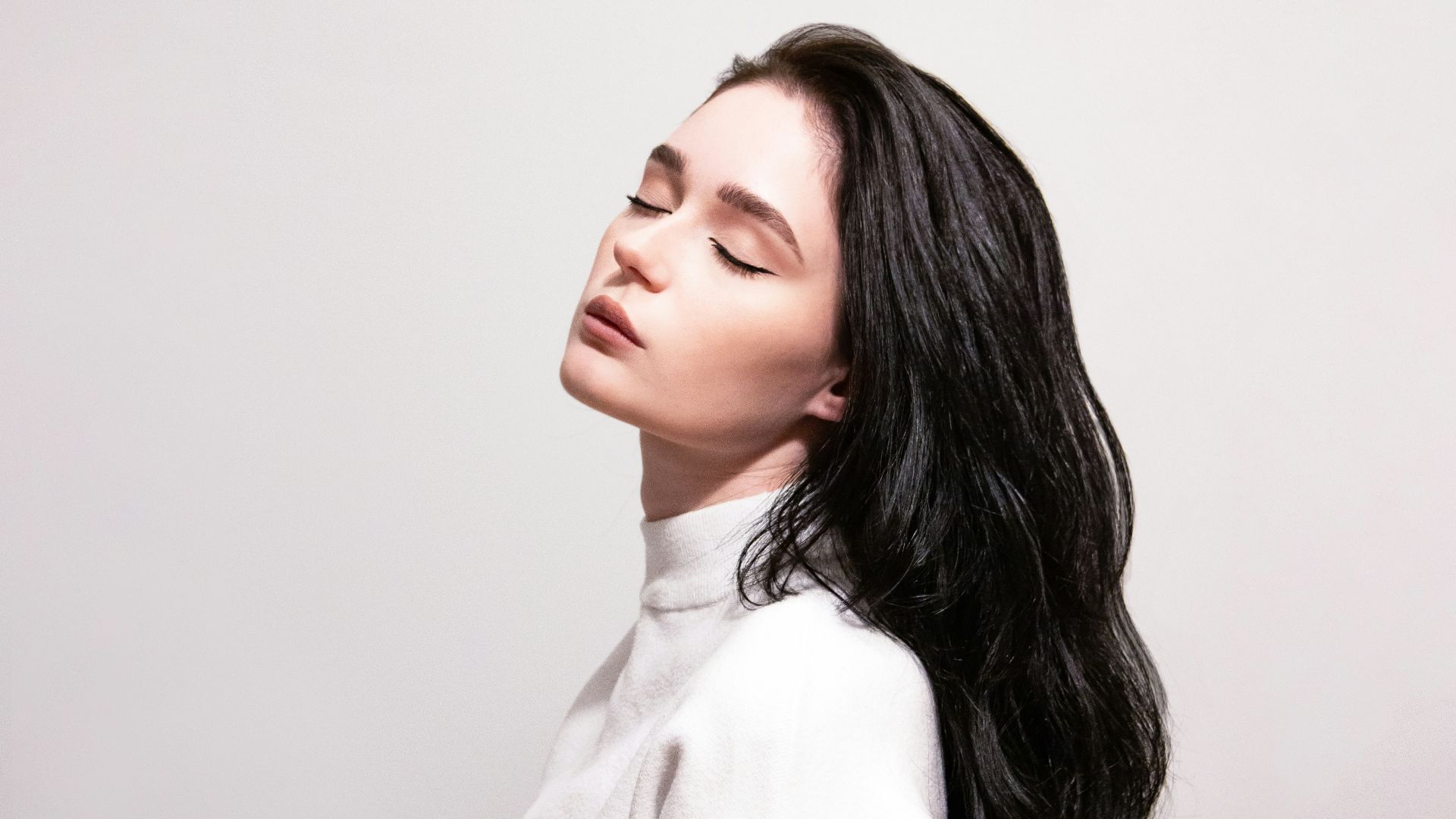 a woman with long black hair standing in front of a wall