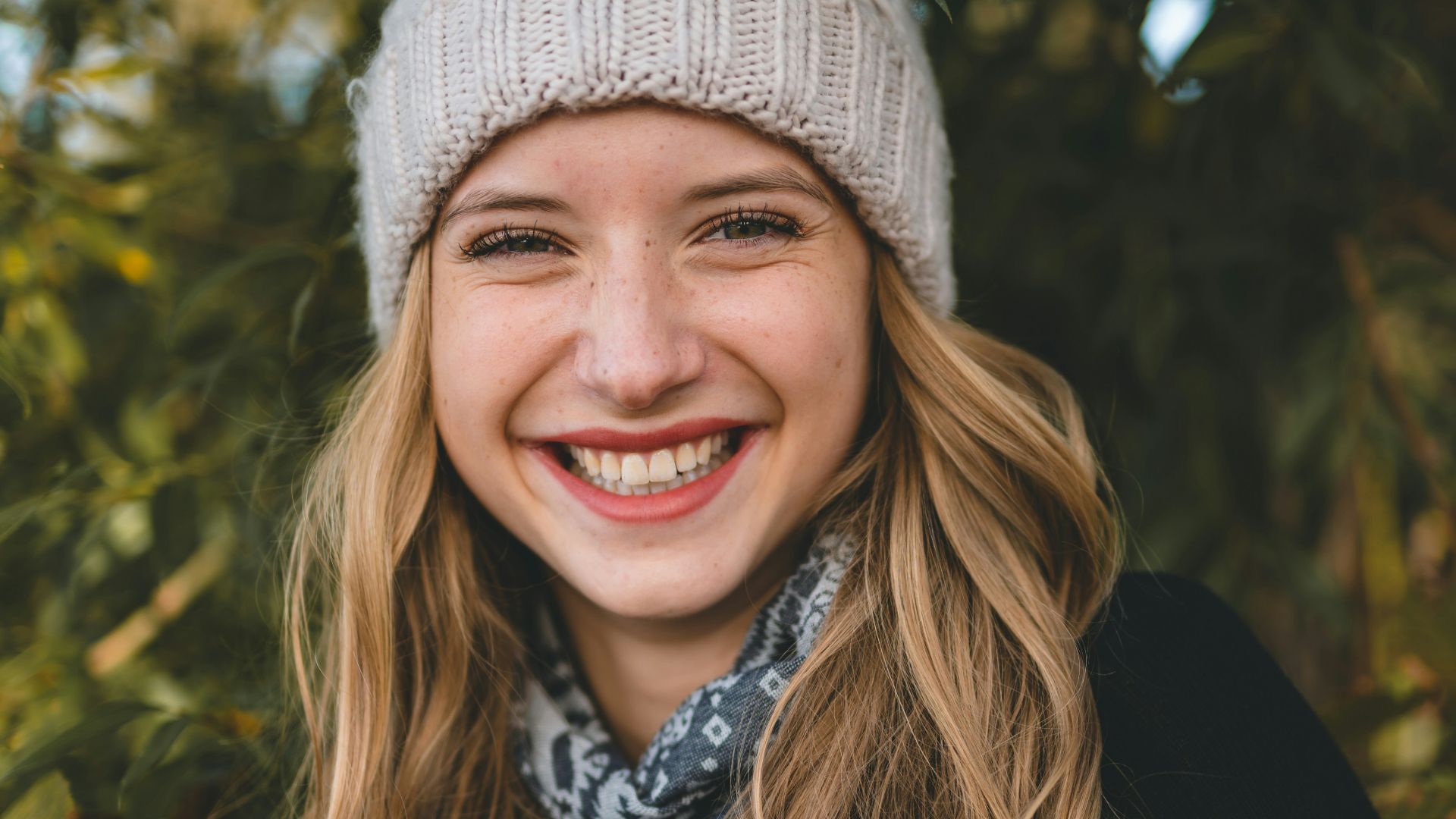 smiling woman in black and white floral shirt wearing gray knit cap