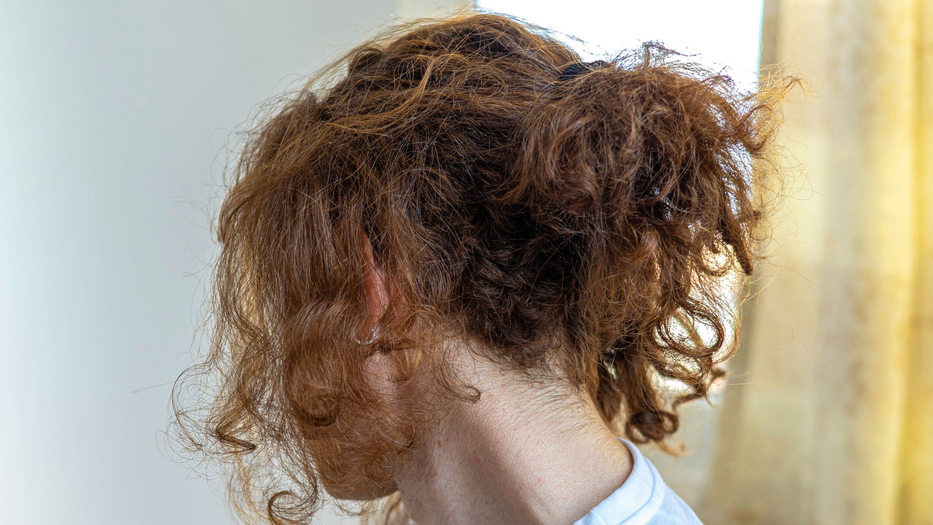 a woman with curly hair sitting in front of a window