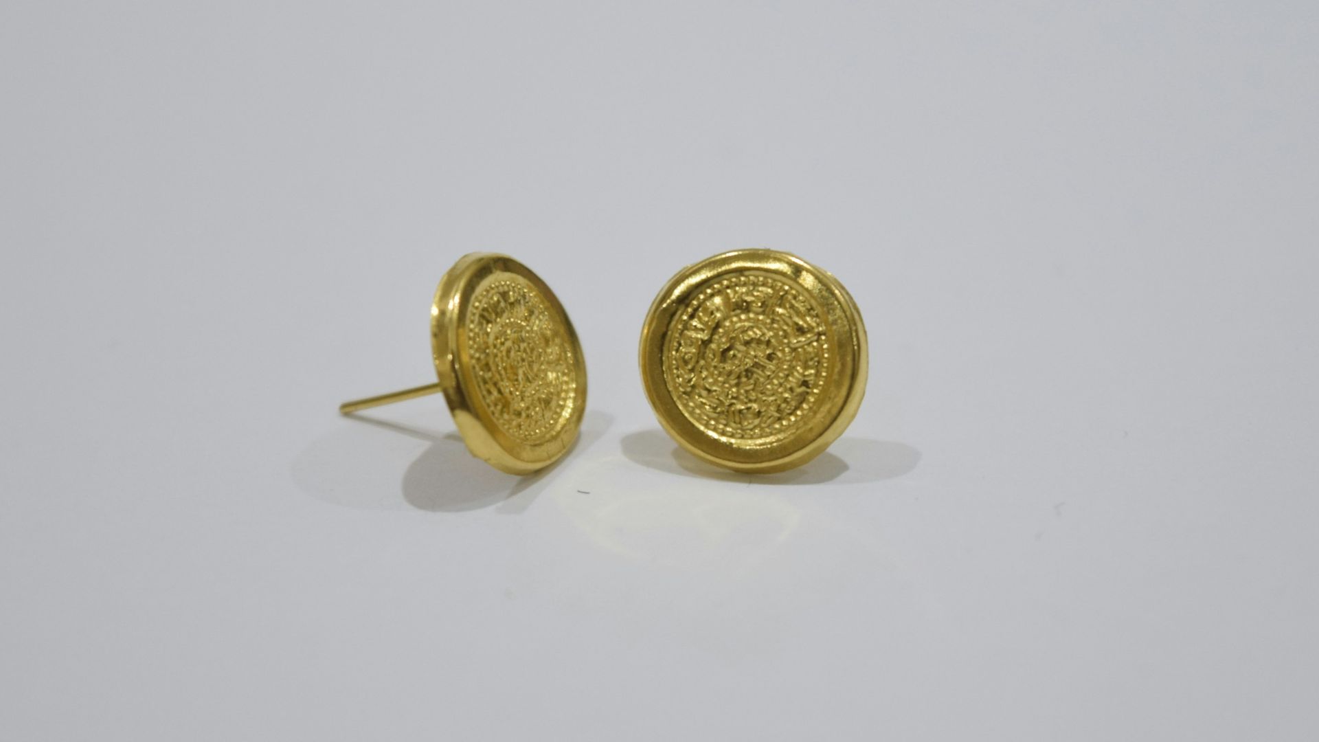 Two gold stud earrings with embossed designs.