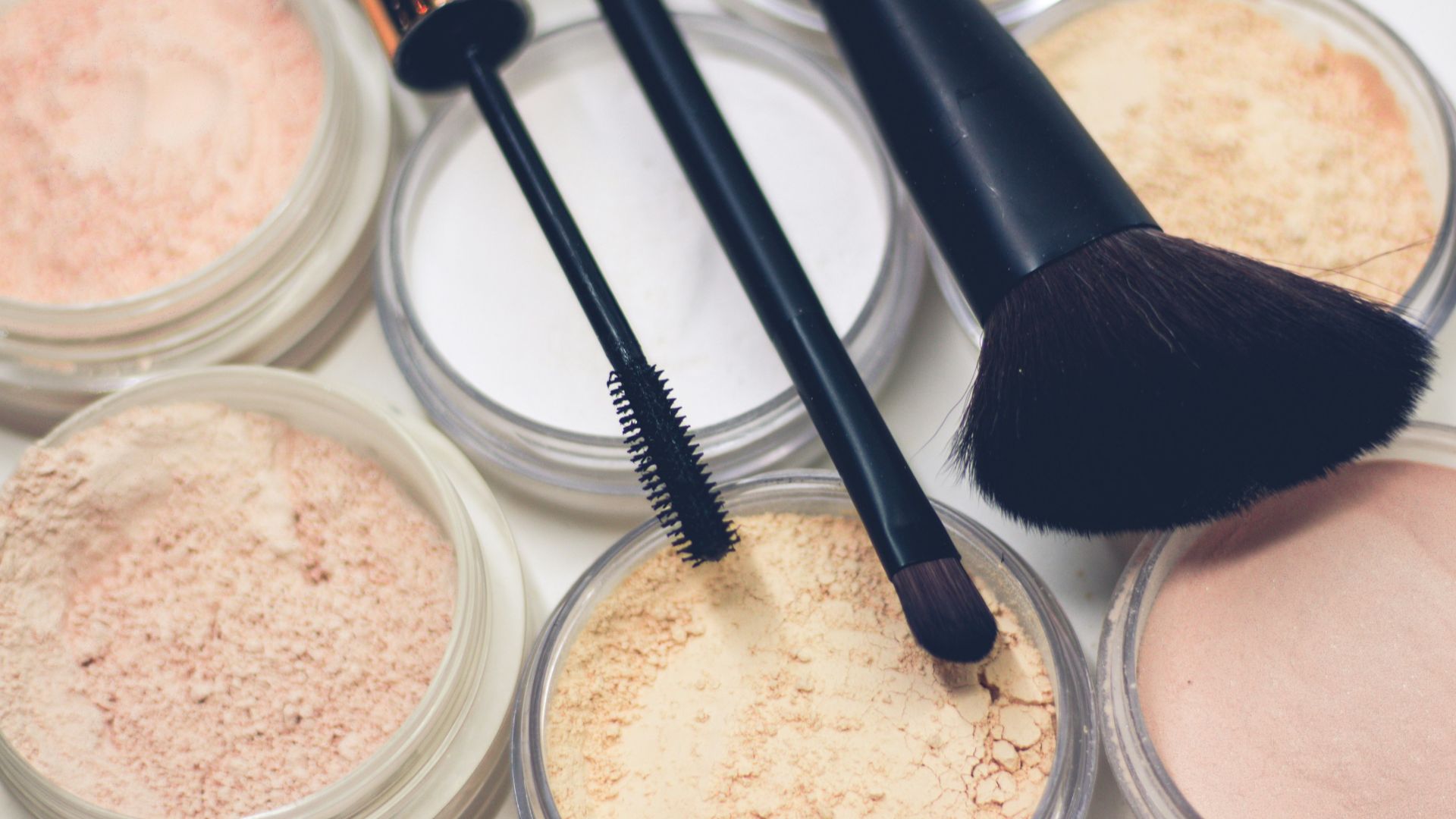 three makeup brushes on top of compact powders