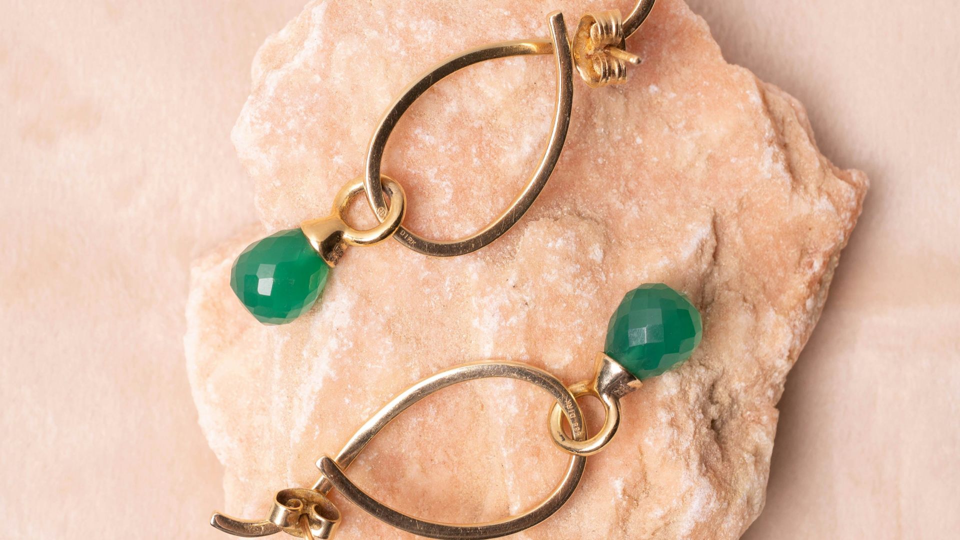 Gold earrings with green gemstones on pink stone
